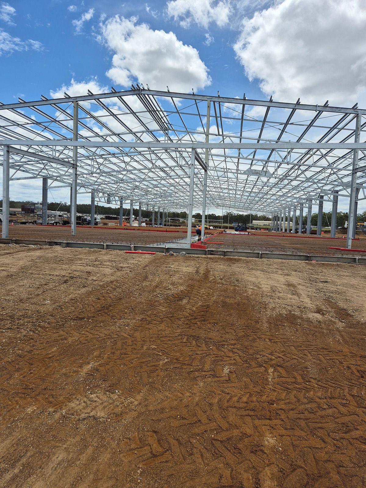 Steel Frame Building Under Construction on a Dirt Lot Beneath a Cloudy Blue Sky — TP Concreting In Warilla, NSW