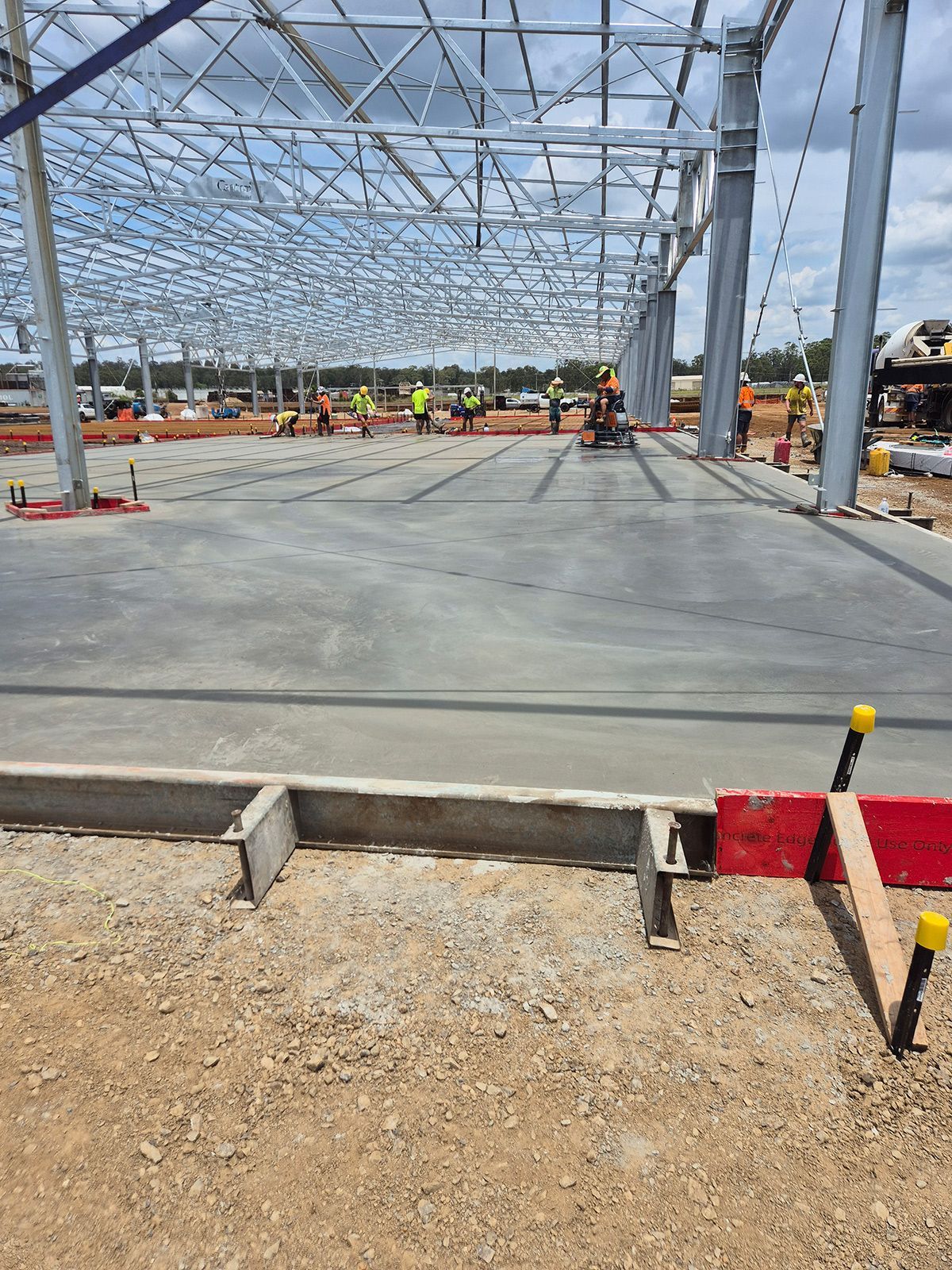 Construction Workers on a Steel-framed Building Site With a Newly Poured Concrete Slab — TP Concreting In Warilla, NSW