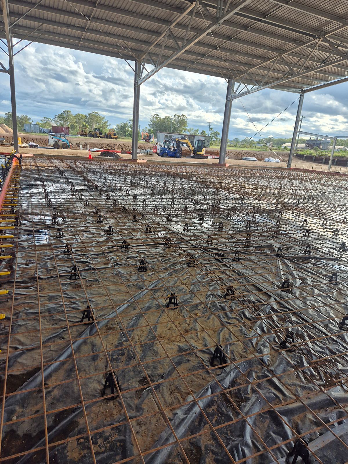 Construction Site With Rebar Mesh and Concrete Slab Under a Steel-roofed Structure — TP Concreting In Warilla, NSW