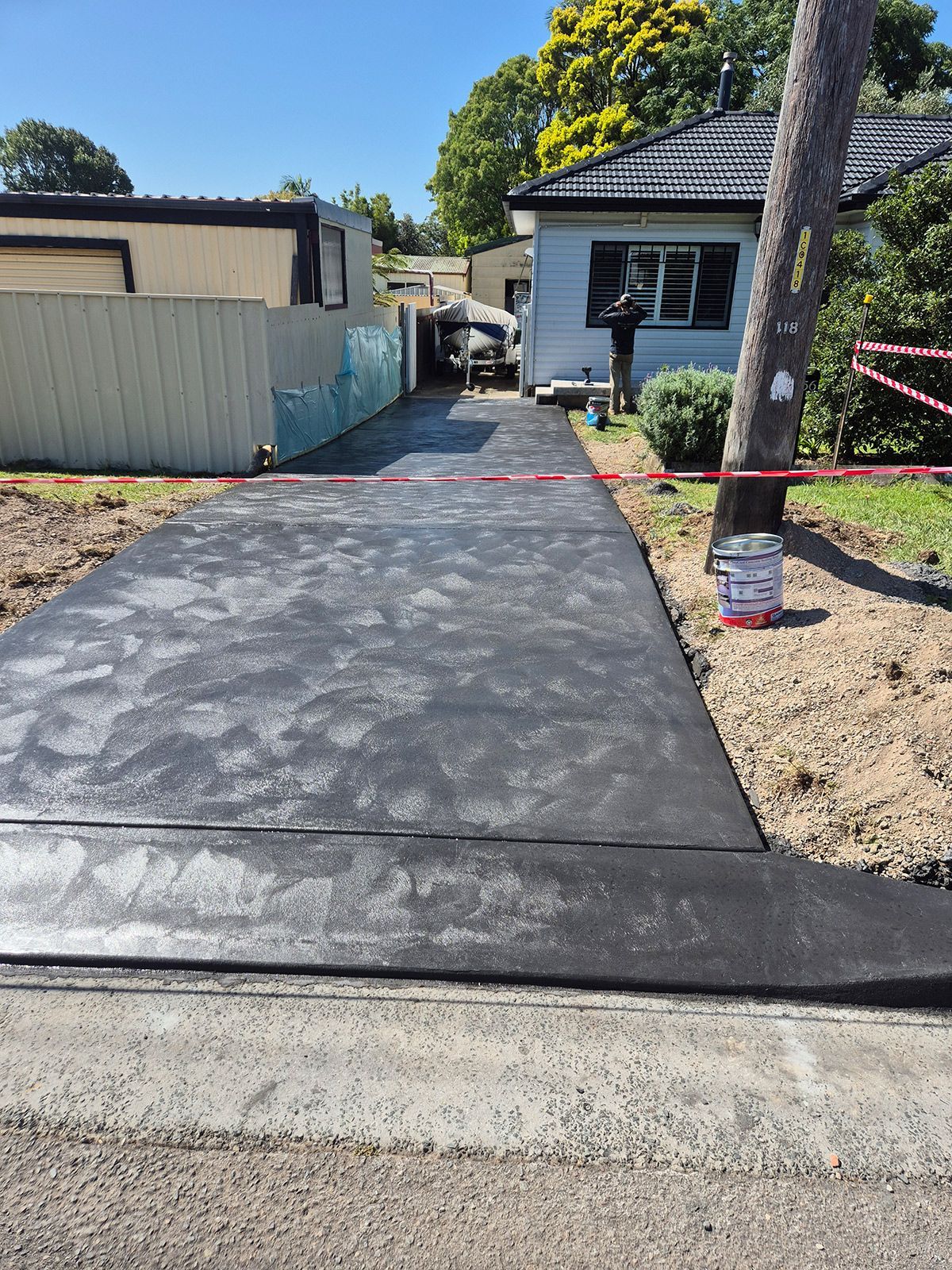 Freshly Poured Concrete Driveway Leading to a House, With a Utility Pole and Fenced Side Yard — TP Concreting In Warilla, NSW