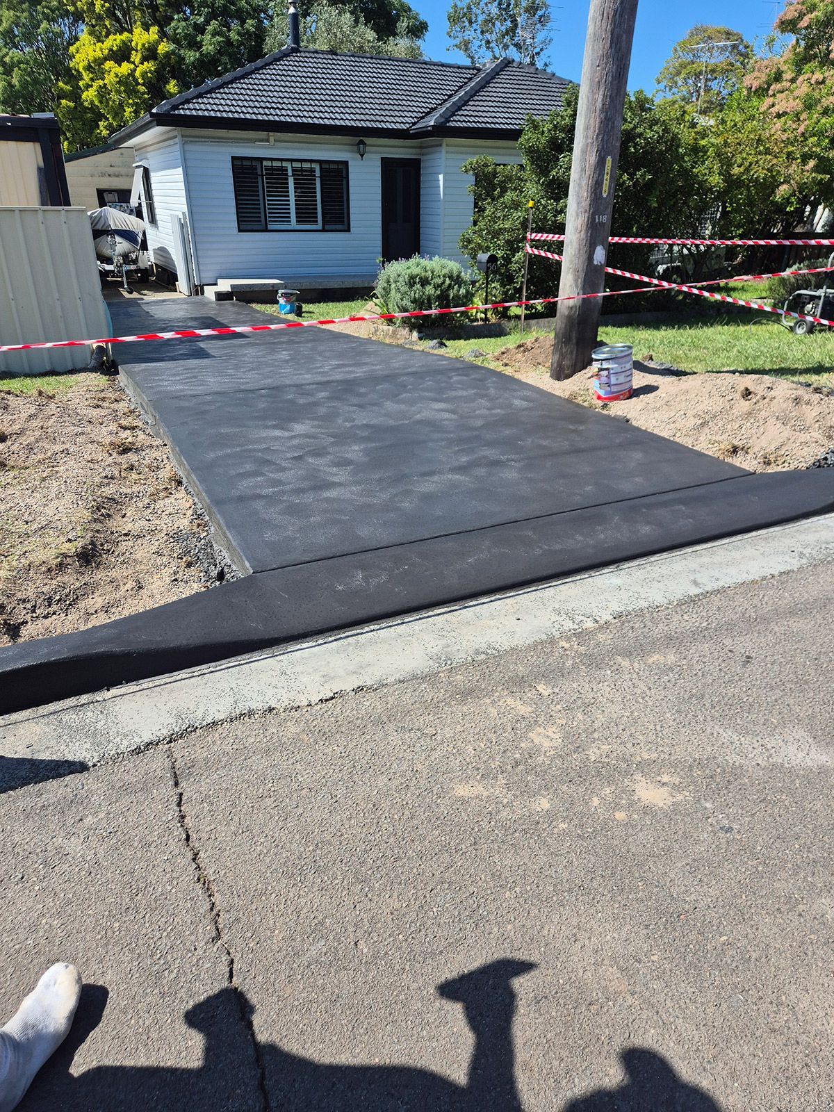Freshly Paved Black Driveway Leading to a Small White House With Red Caution Tape — TP Concreting In Warilla, NSW