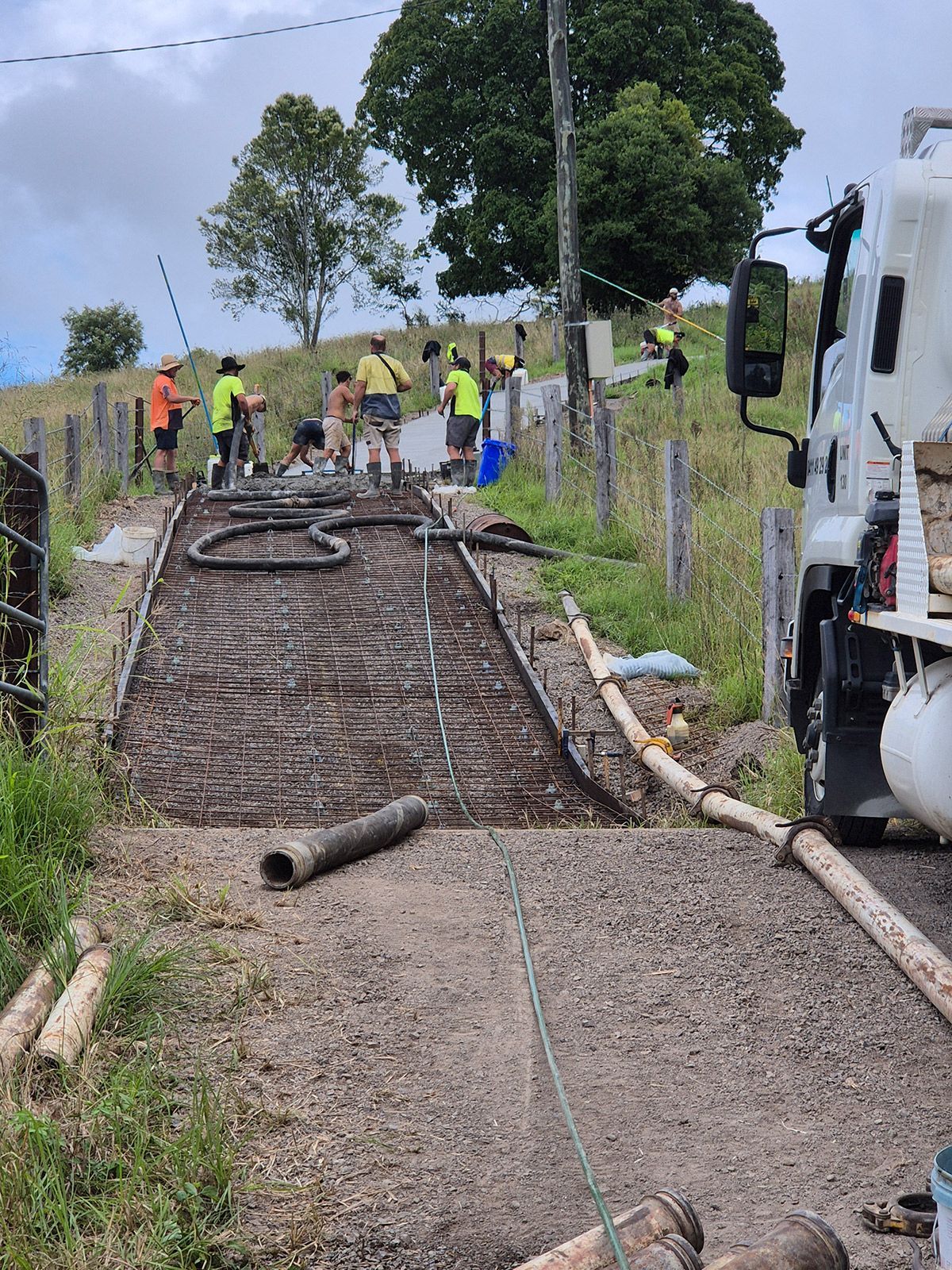 Workers Paving a Steep Rural Road Beside a Truck, With Fencing and Trees on Both Sides — TP Concreting In Warilla, NSW