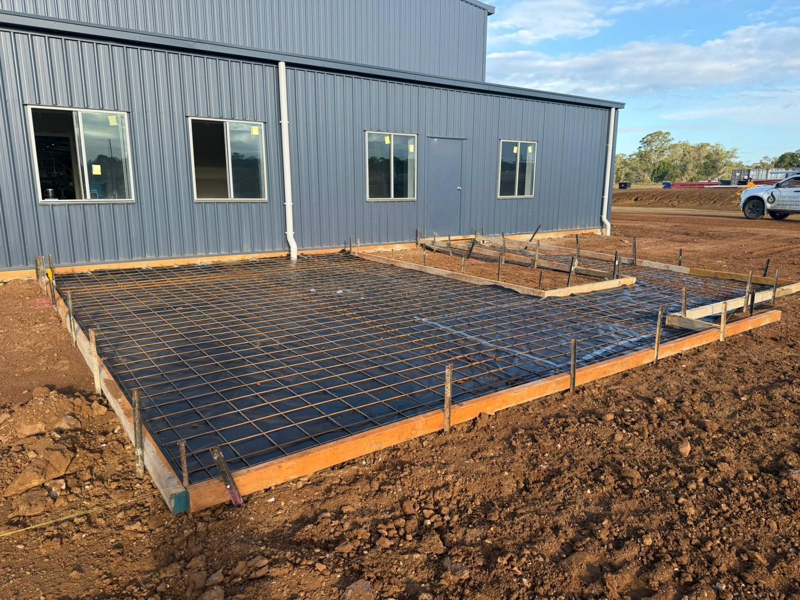 Concrete Foundation Rebar Grid Beside a Gray Metal Building Under Construction — TP Concreting In Warilla, NSW