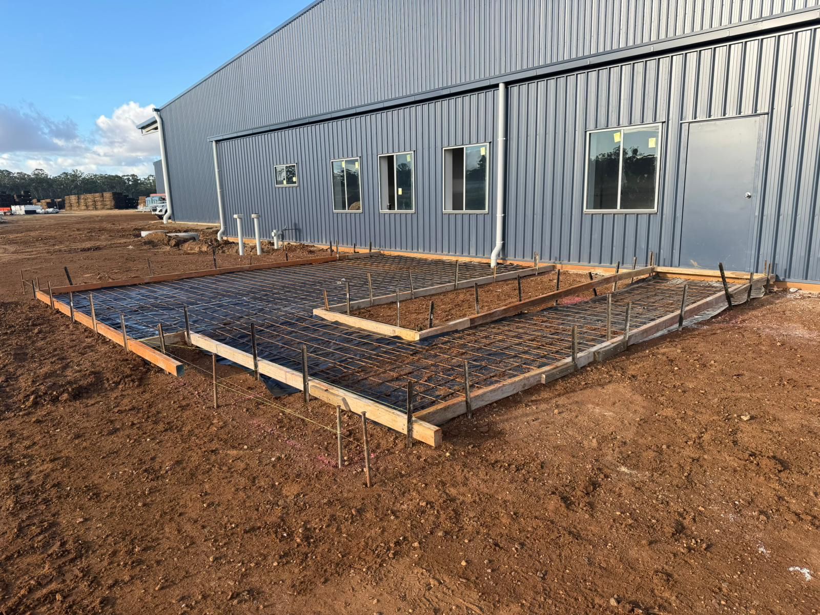 Concrete Foundation Forms Beside a Gray Metal Building on a Dirt Construction Site — TP Concreting In Warilla, NSW