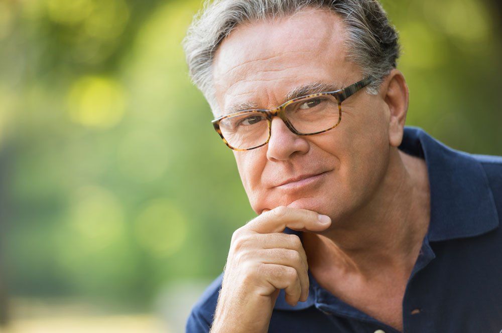 A man wearing glasses is looking at the camera with his hand on his chin.