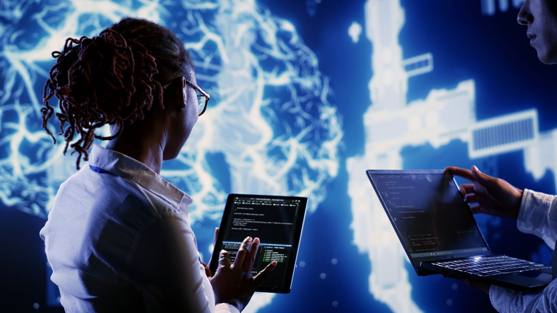 A man and a woman are looking at a tablet and a laptop.