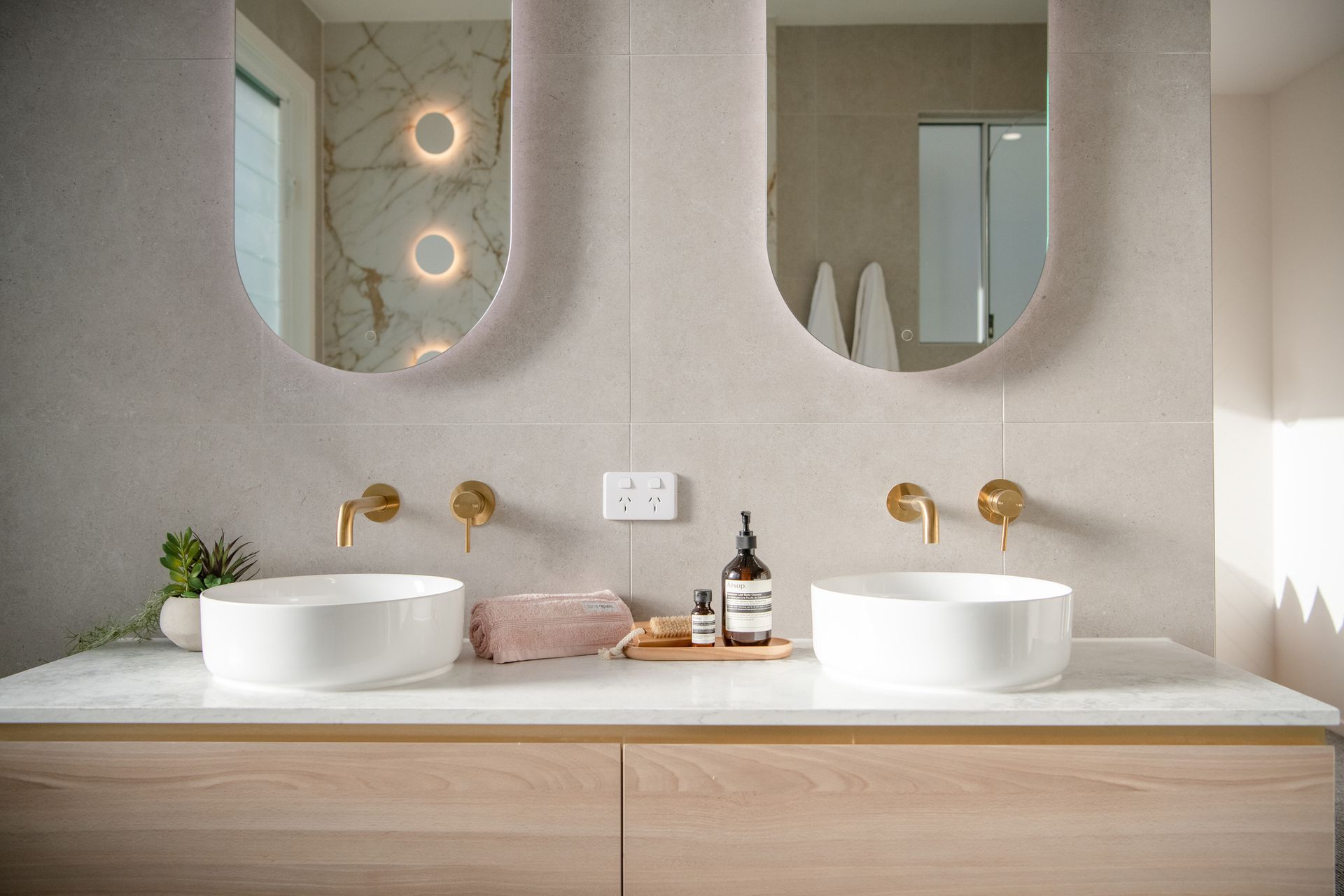 Bathroom with wood cabinets, two arched mirrors, and sconces, with sinks and a tall cabinet.