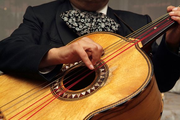 Mariachi musician playing guitar, wearing a sombrero, colorful background.