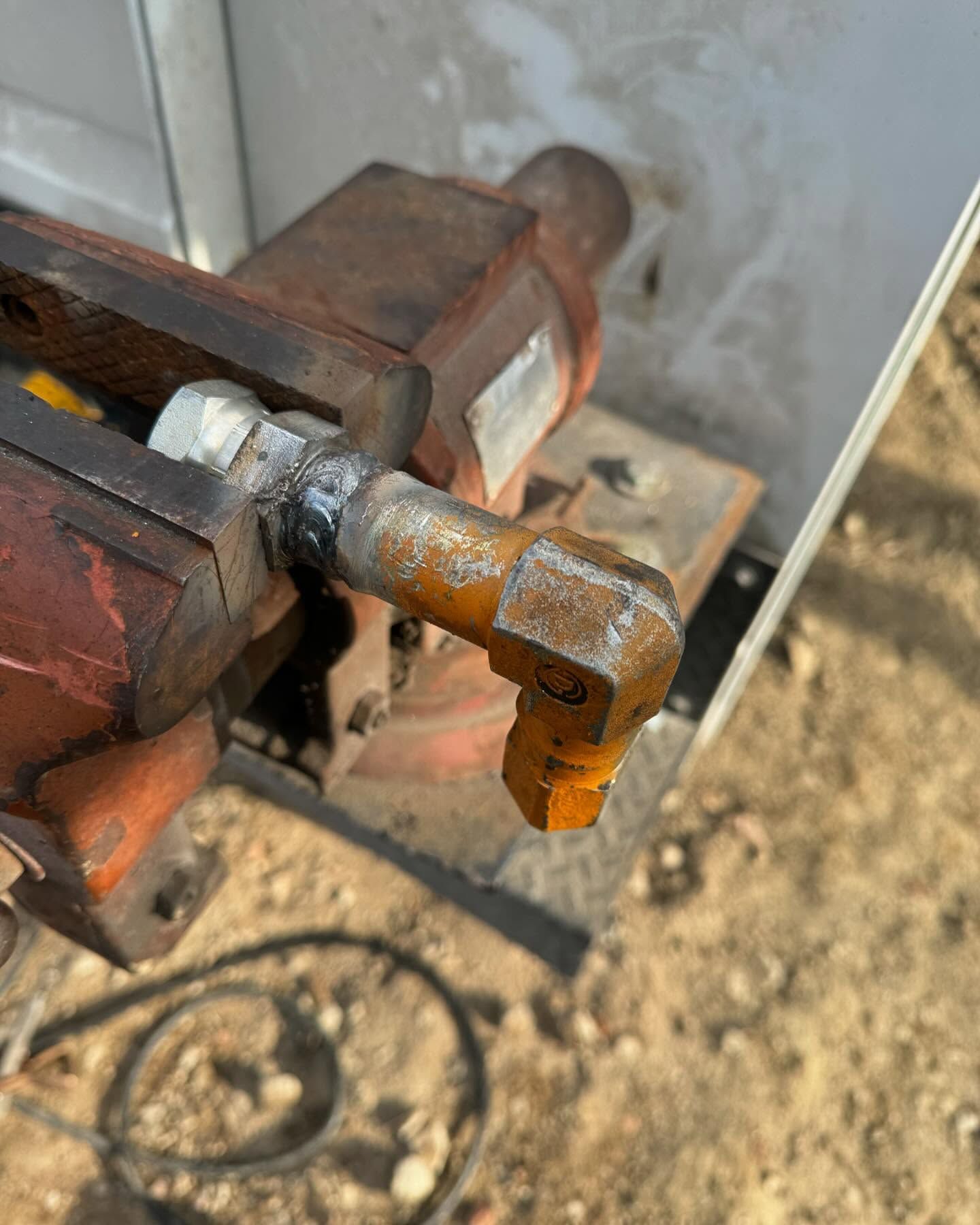 Rusty metal clamp gripping a small cylindrical tool or bolt outdoors on a dirt surface