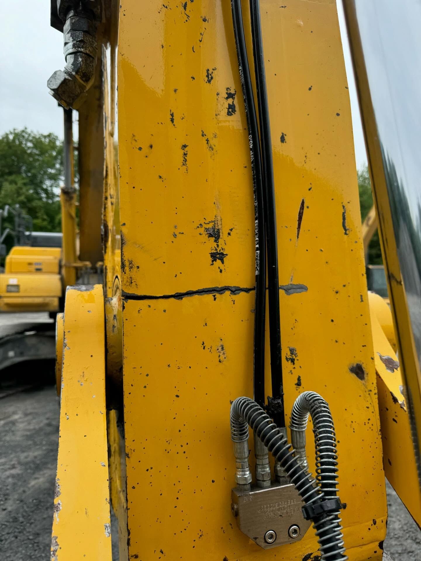 Close-up of a yellow construction machine arm with black scuffs and a coiled hose connector.