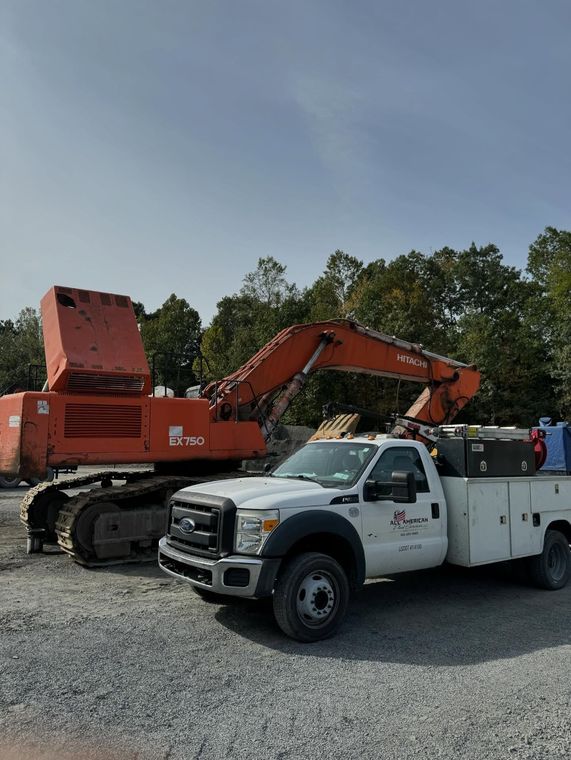 White utility truck beside orange excavators on gravel lot under clear sky