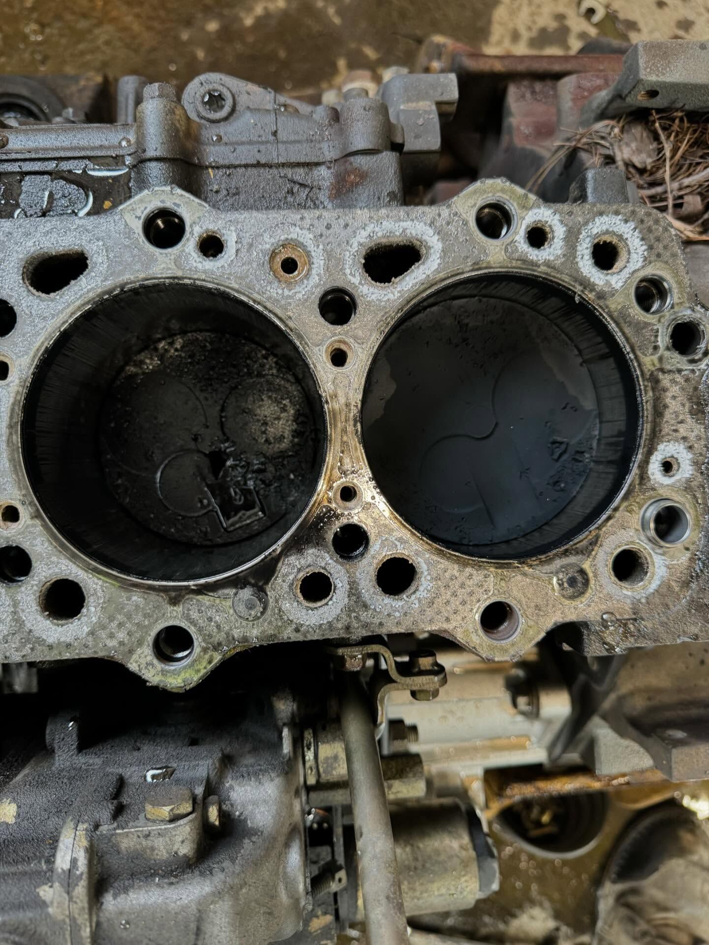 Close-up of a damaged engine cylinder head with two soot-covered chambers and gasket holes