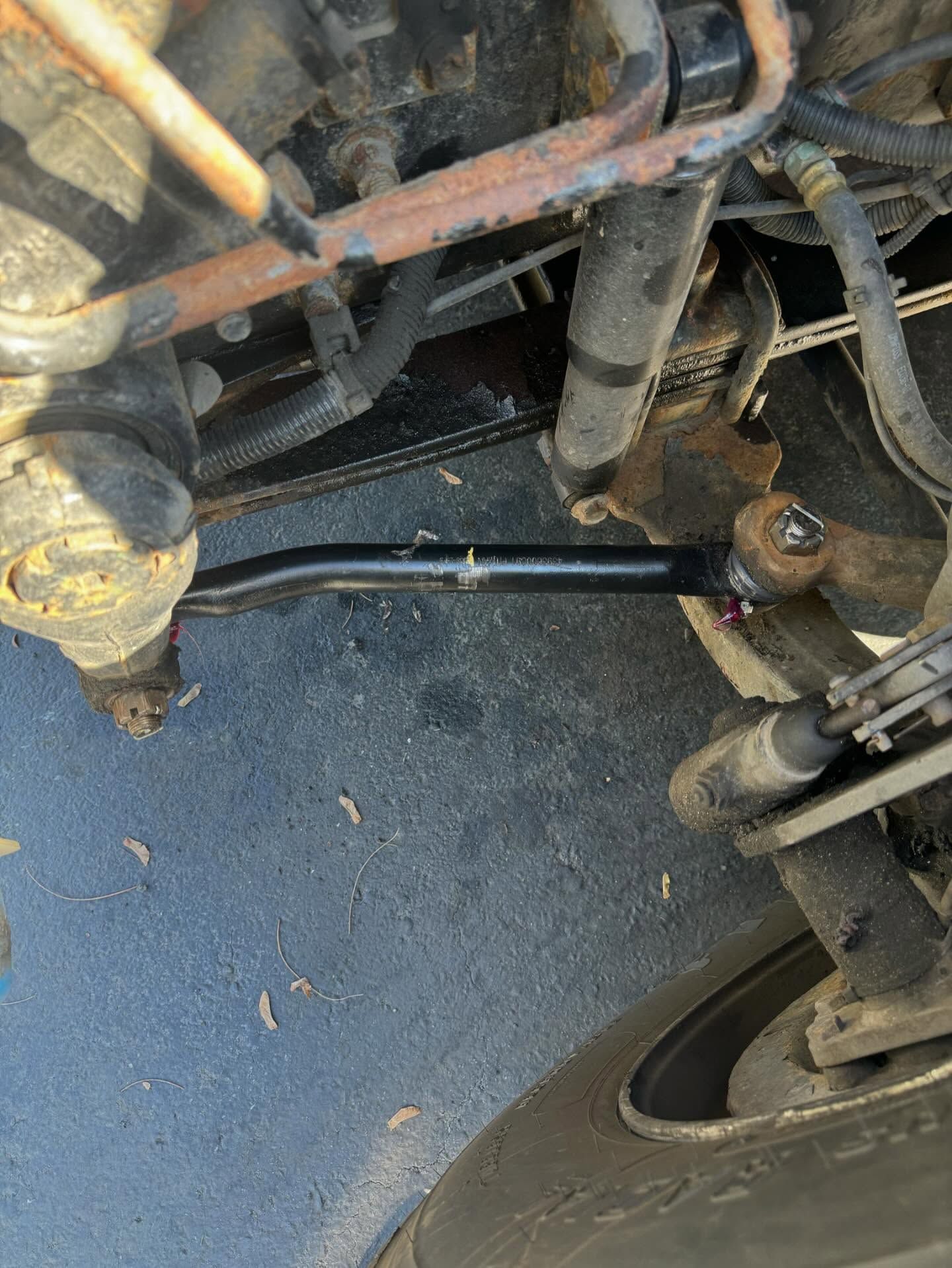 Close-up of a vehicle’s front suspension and steering components with a black tie rod near the wheel.