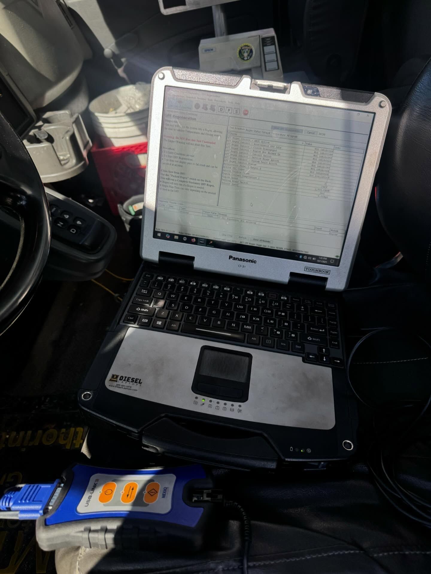 Laptop with a spreadsheet open, mounted in a vehicle dashboard area.