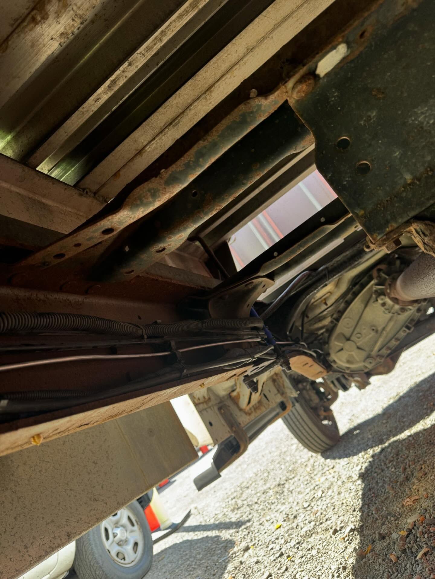 Undercarriage of a vehicle lifted on a tow truck, showing metal frame and wheel area.