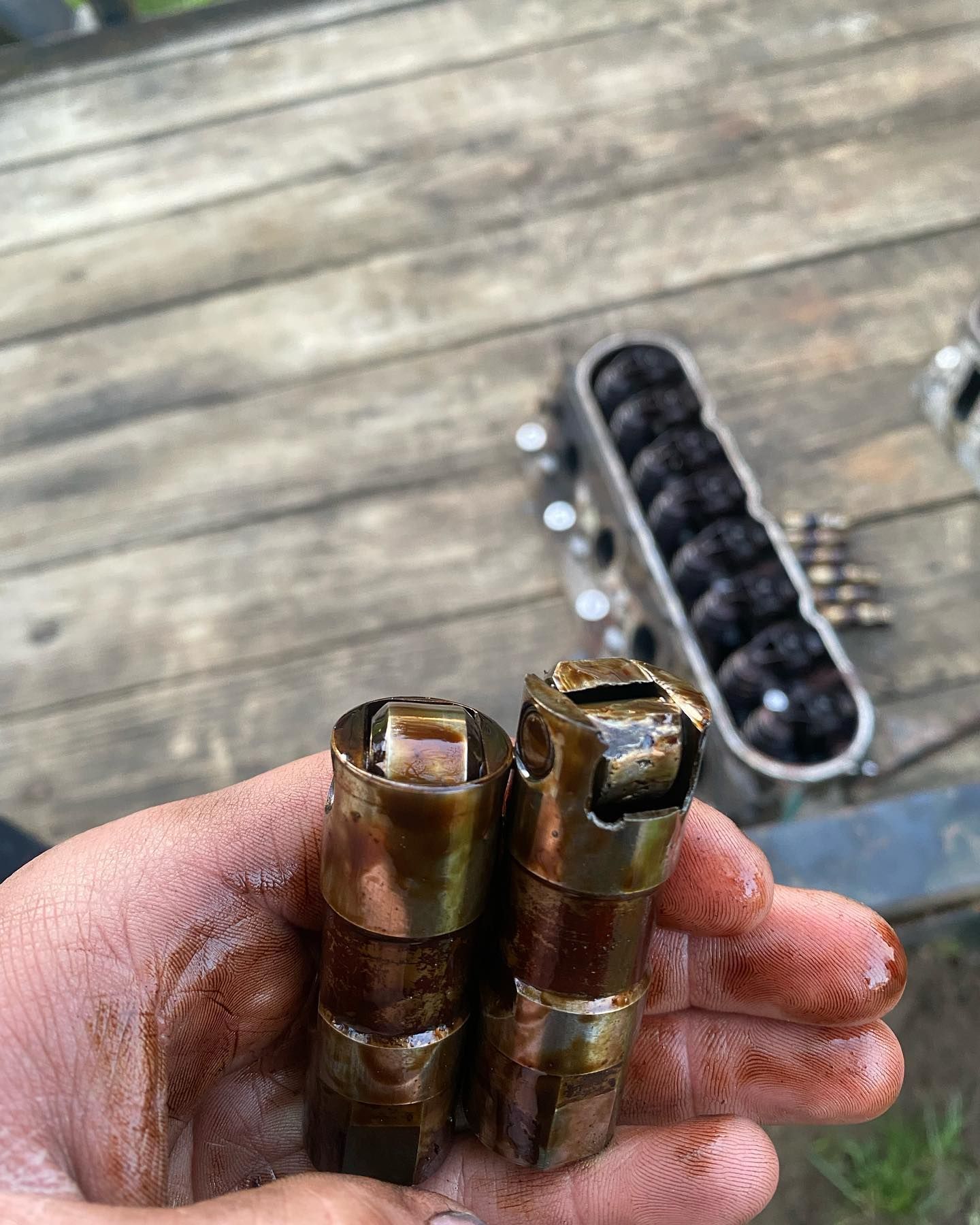 Hand holding two brass cartridges with damaged tops, with a box of dark rounds on a wooden deck in the background