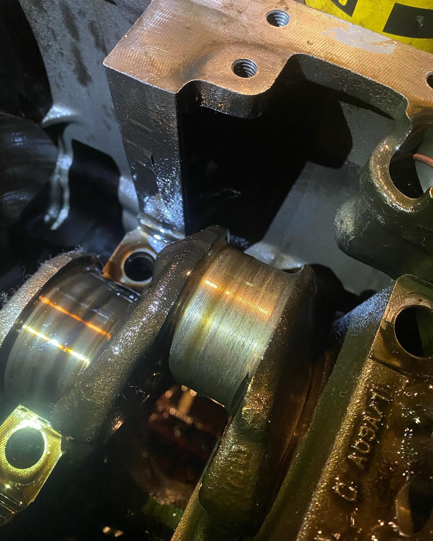 Close-up of shiny metal engine camshaft journals and block inside an oily engine bay