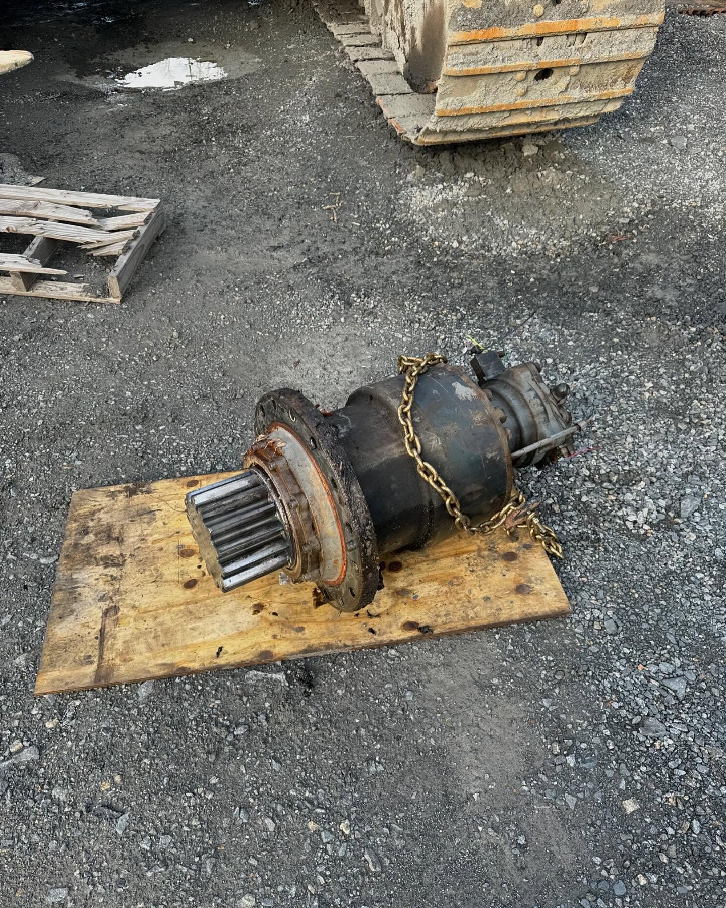 Dirty industrial metal component with chain on a wooden pallet in a gravel yard