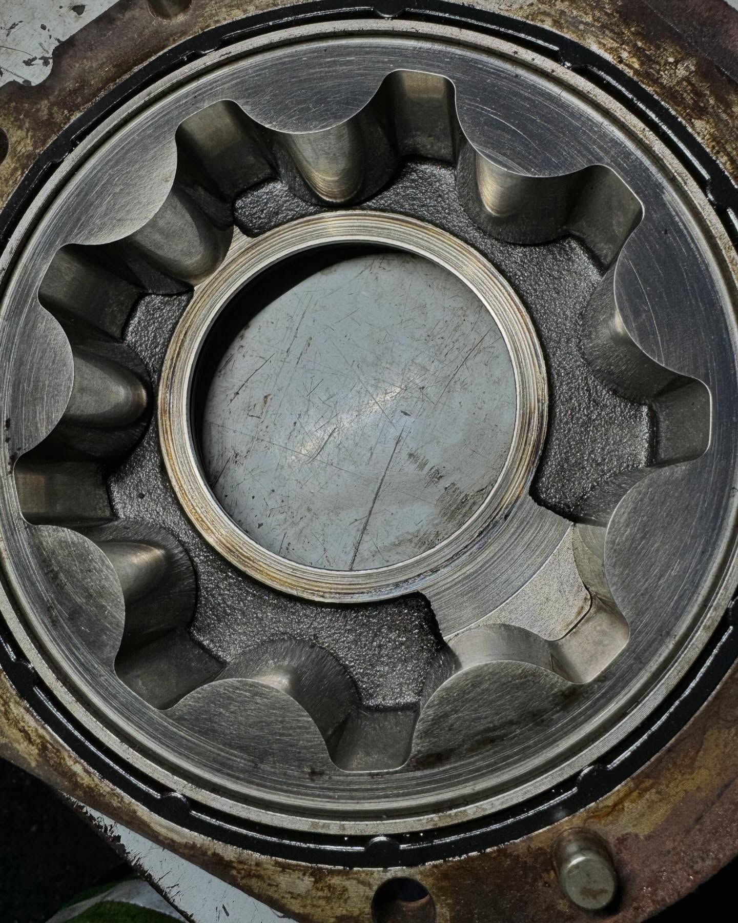 Close-up of a worn metal gear or pump rotor with a circular center, showing dark oil stains and rust.