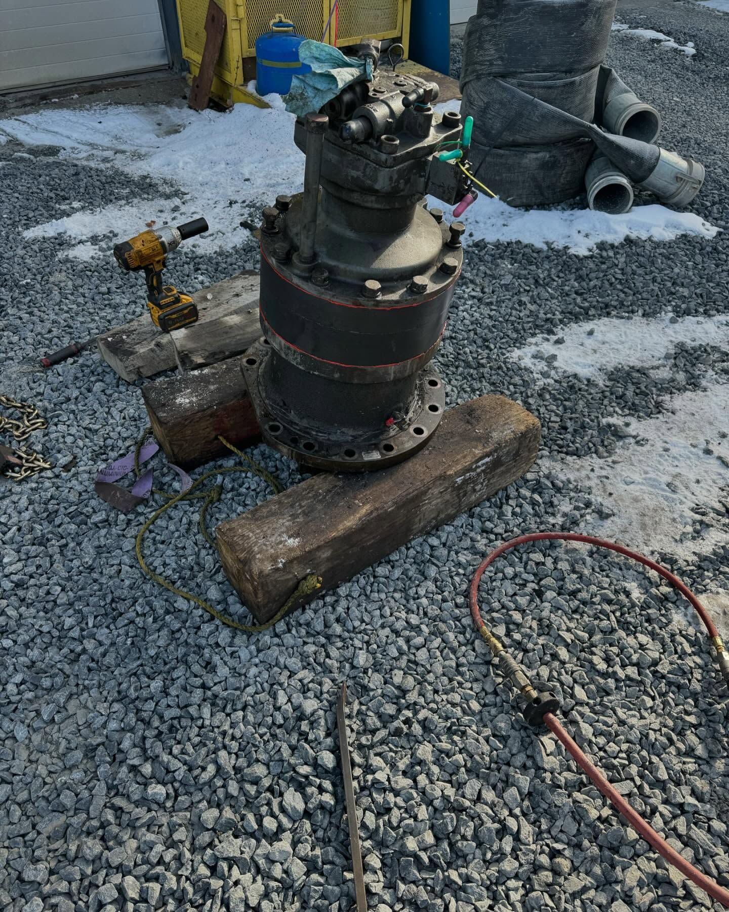 Industrial machine on wooden planks on gravel, with hoses attached outdoors near a work area.