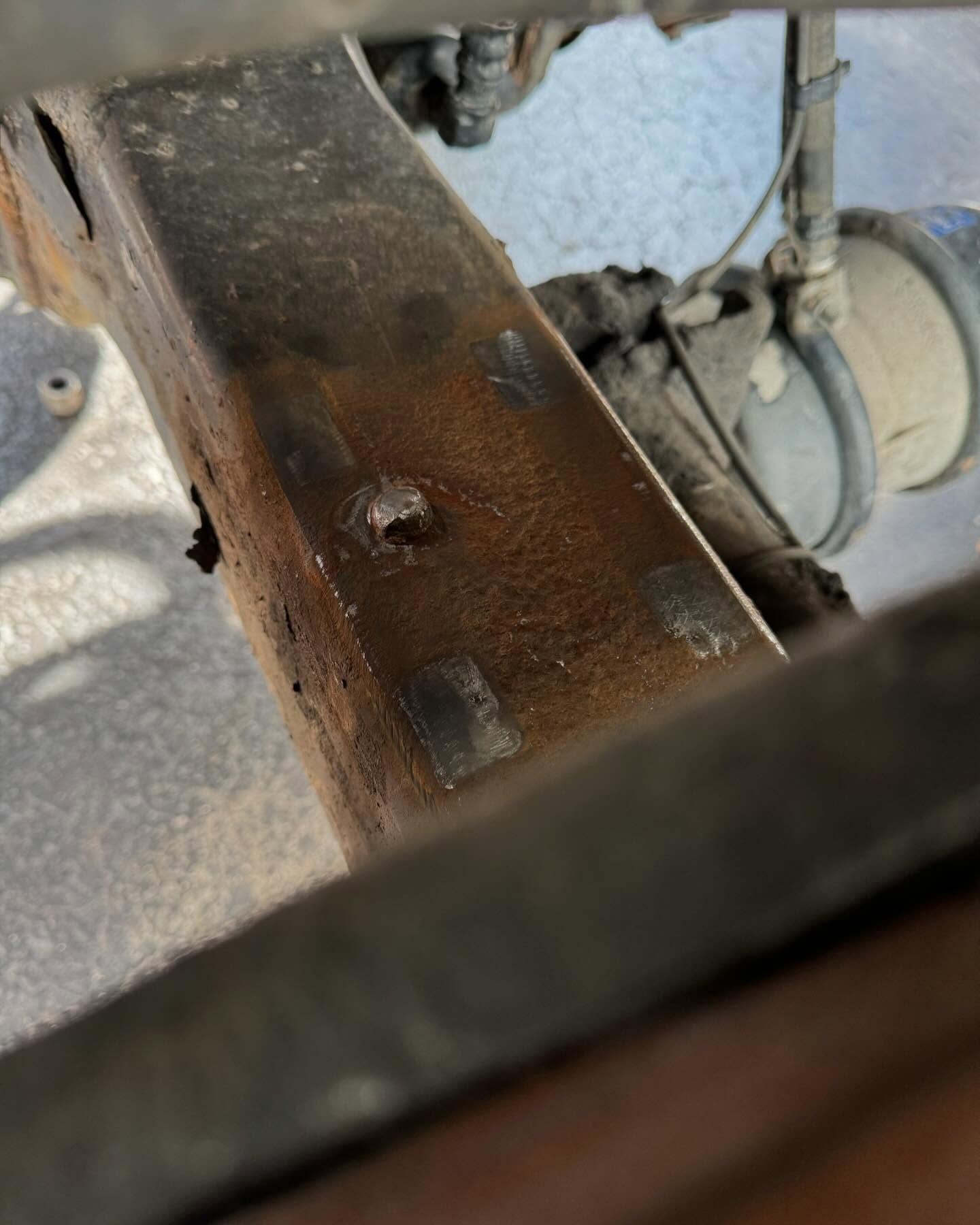 Close-up of a rusted metal beam and wheel assembly with bolts and wiring underneath machinery.