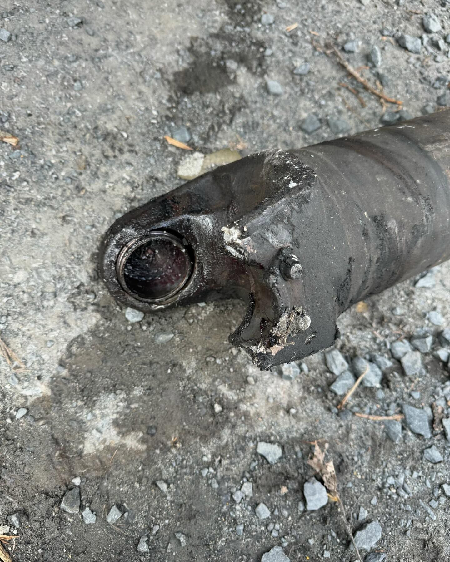 Charred black pipe or hose end lying on gravel, with a broken opening exposed