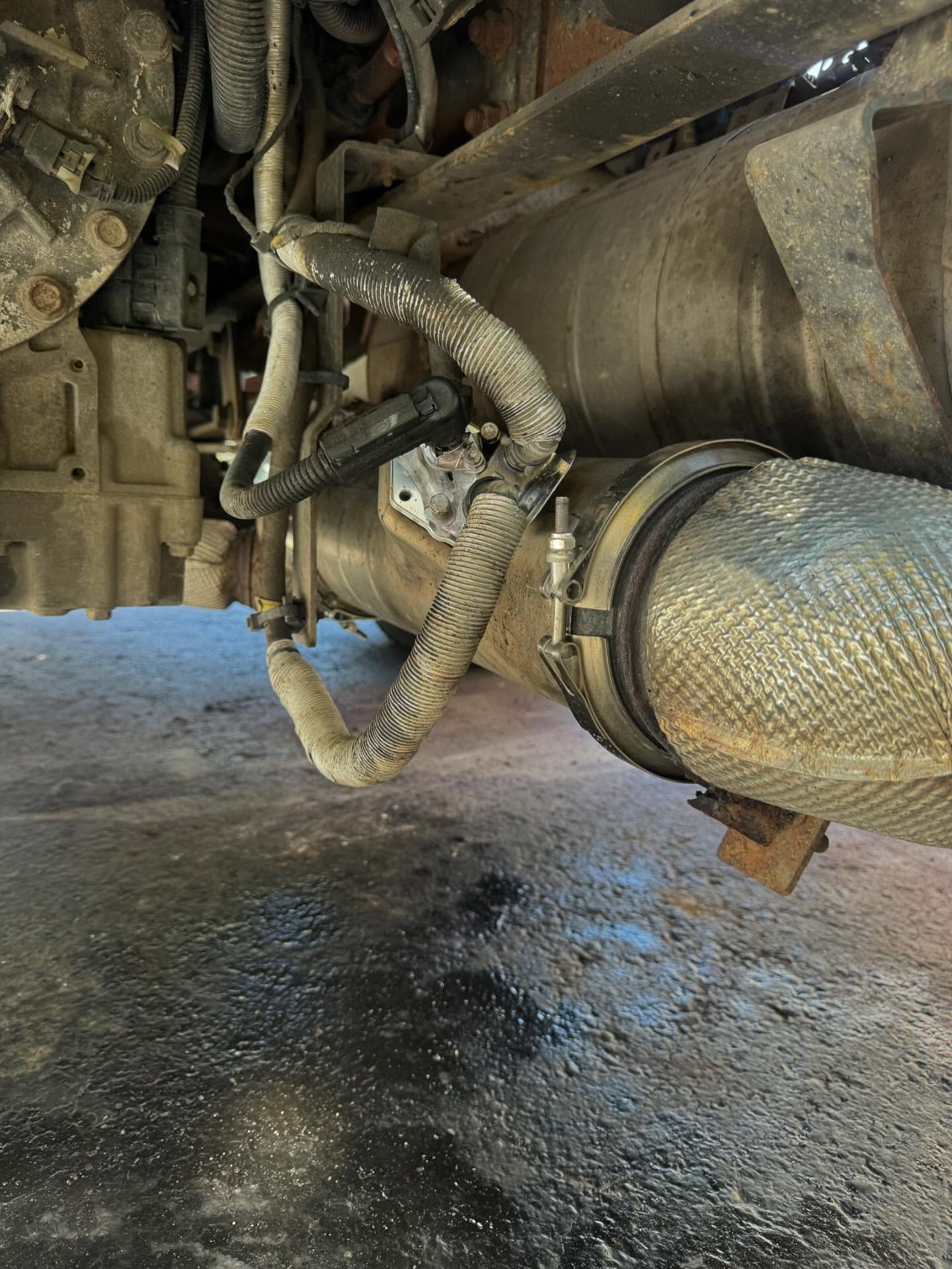 Undercarriage of a vehicle showing a wrapped hose and metal piping near an exhaust system.