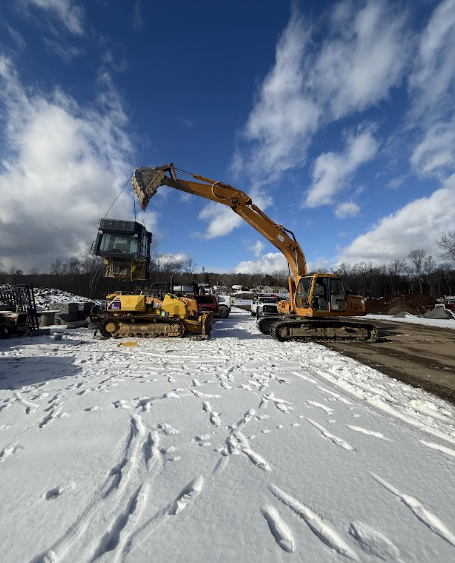 Excavator and construction machine in a snowy worksite under a cloudy blue sky
