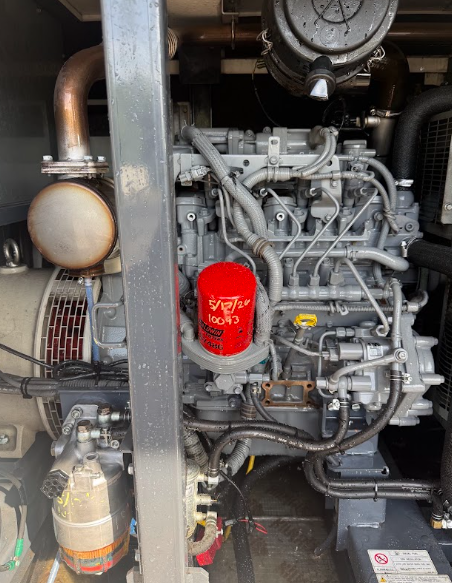 Engine compartment with red oil filter and visible hoses, pipes, and metallic components.