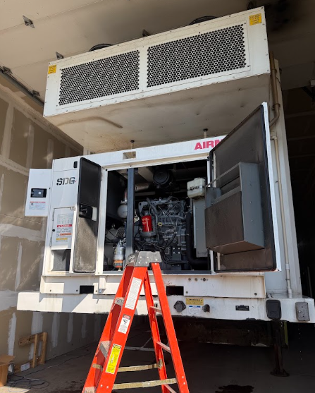 Red-and-white generator on a truck with open doors, viewed from a ladder in a garage.