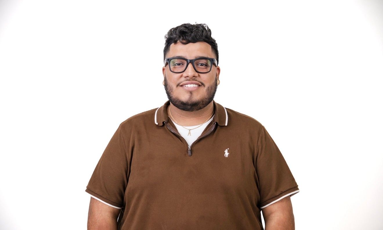 Man with glasses and brown polo shirt smiles against a white backdrop.