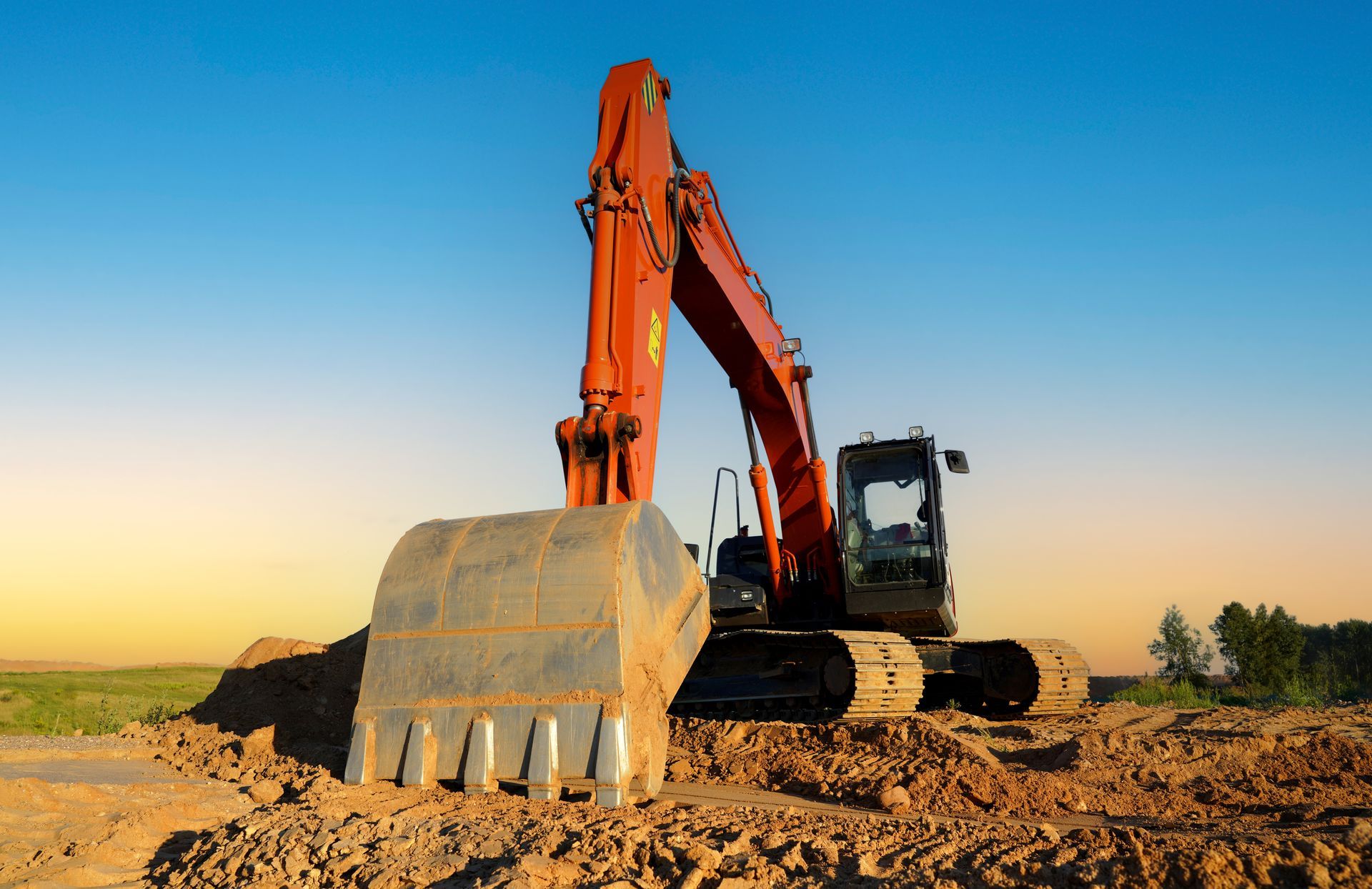 Orange excavator digging dirt at a construction site under a clear blue sky