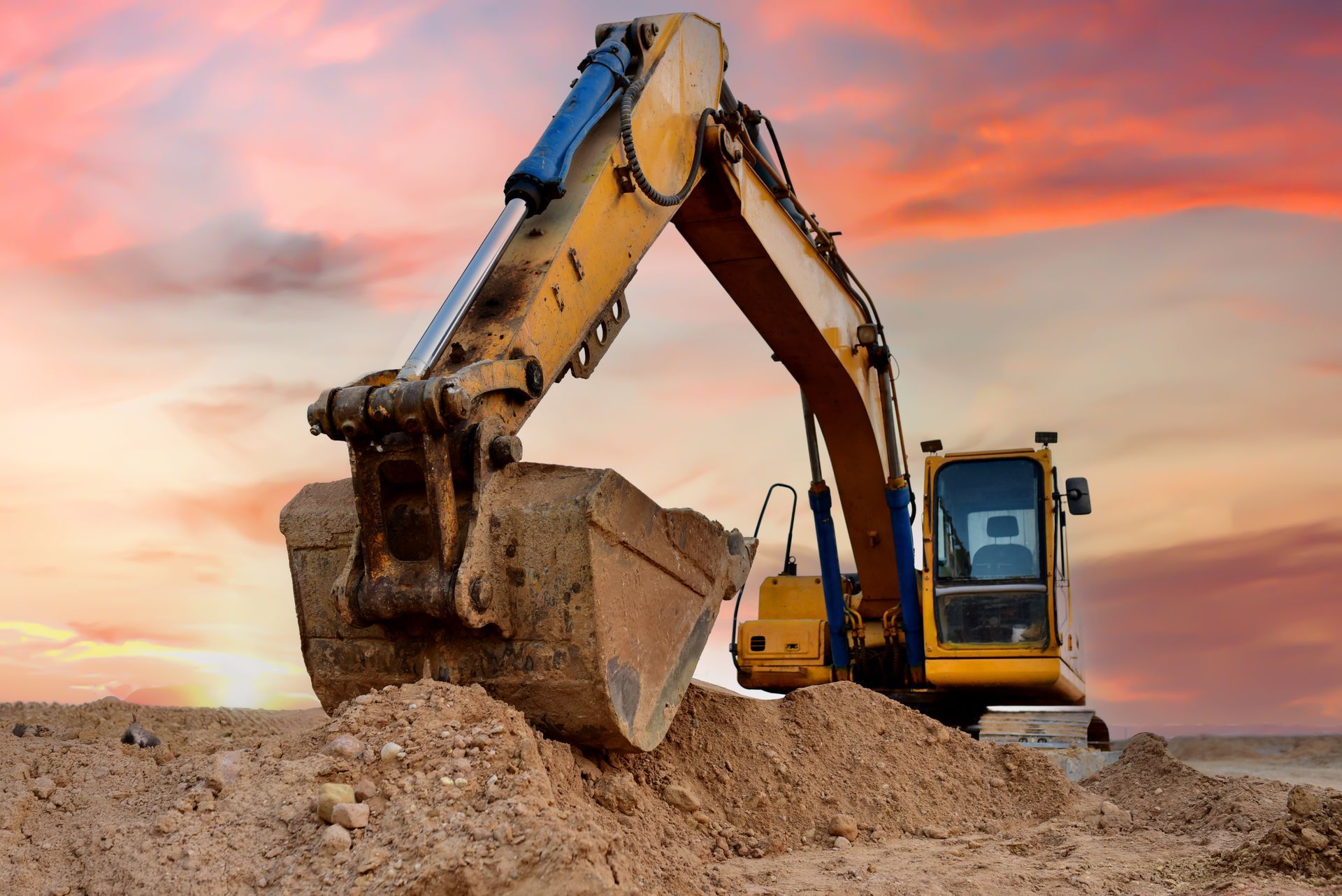 Yellow excavator digging dirt at sunset on a construction site.