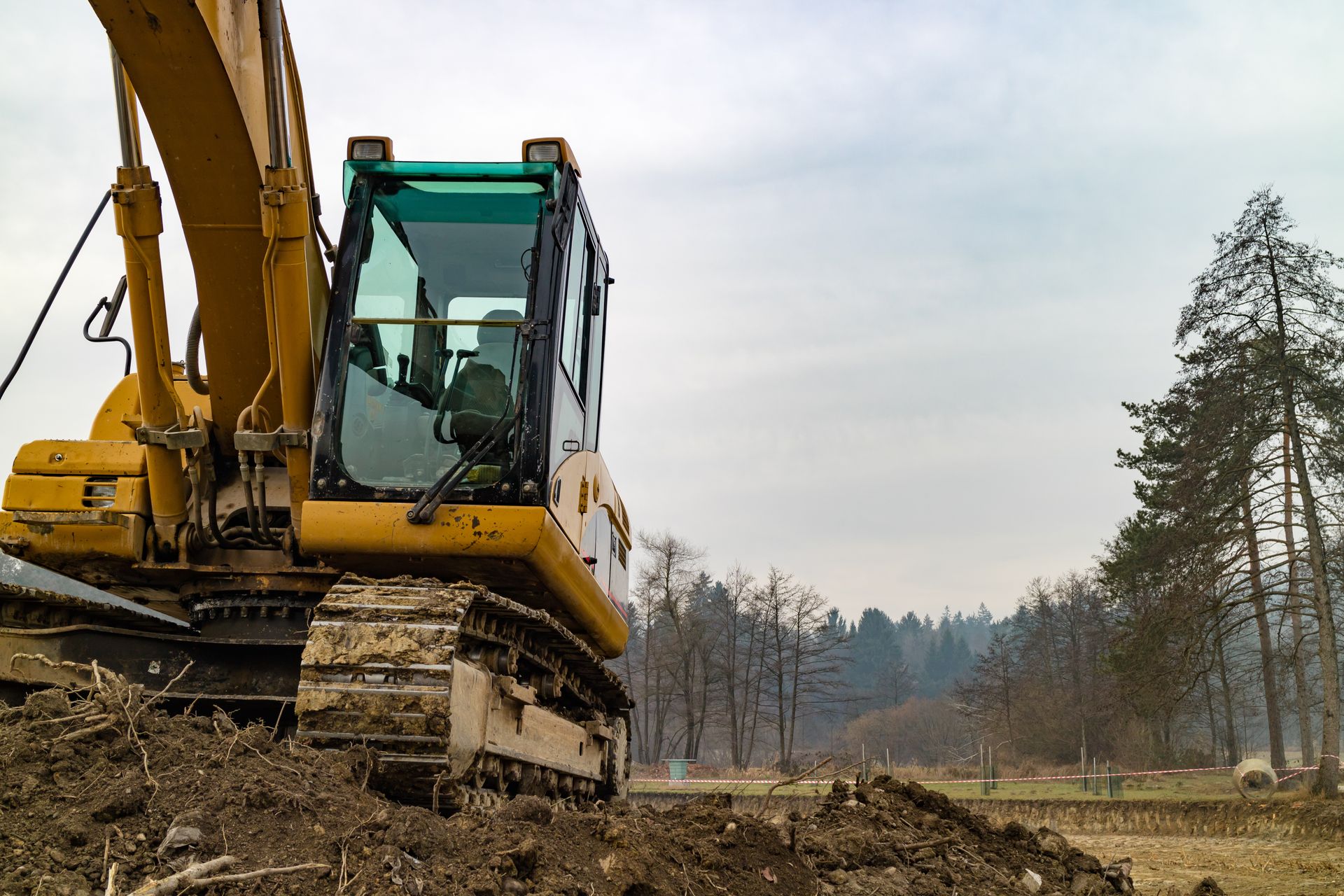 Yellow excavator on muddy ground at a construction site near a tree line