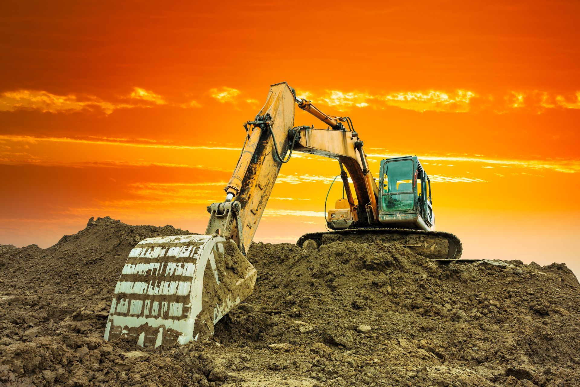 Excavator digging dirt at a construction site under an orange sunset sky