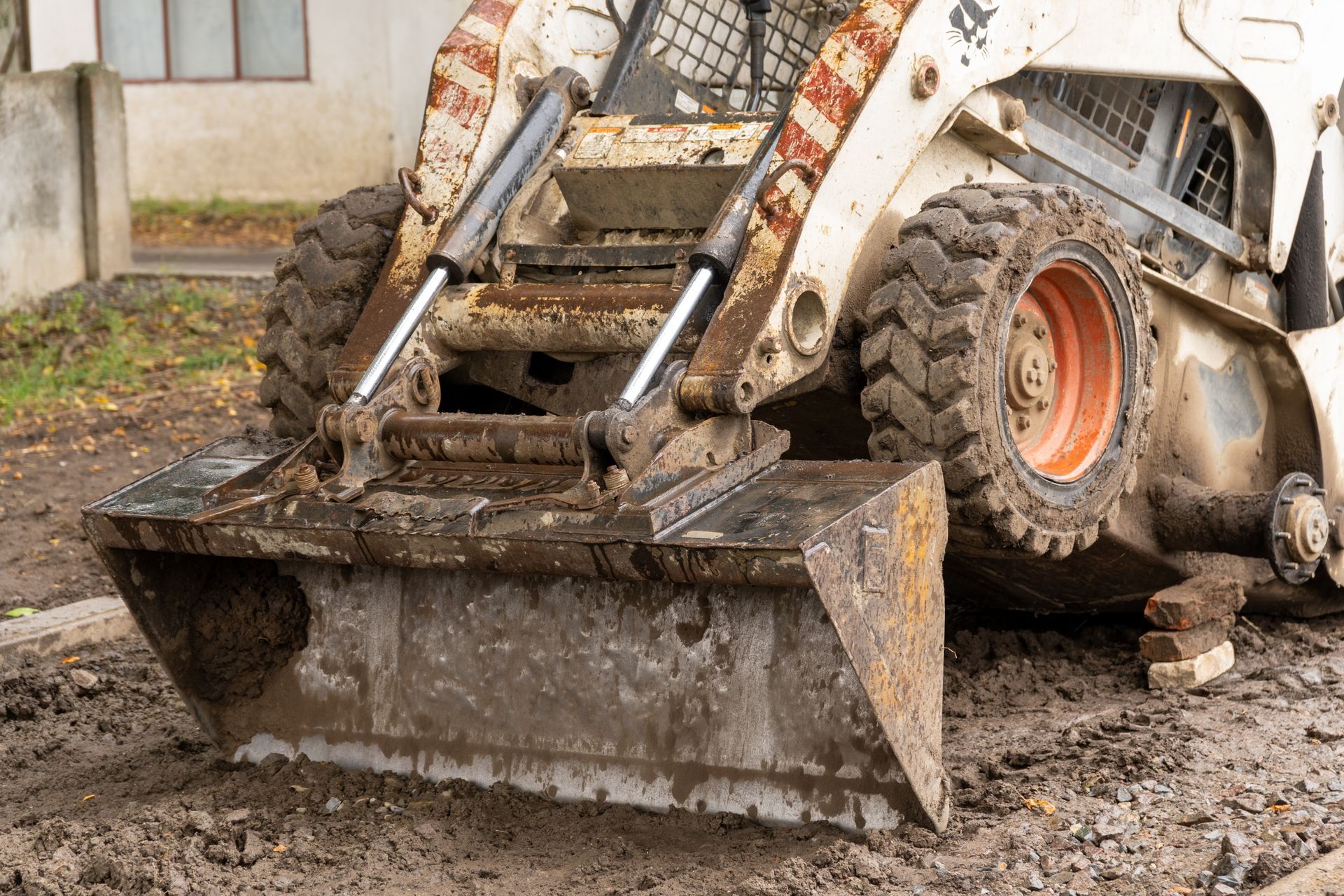 Mud-covered front loader bucket digging through wet soil near a construction site