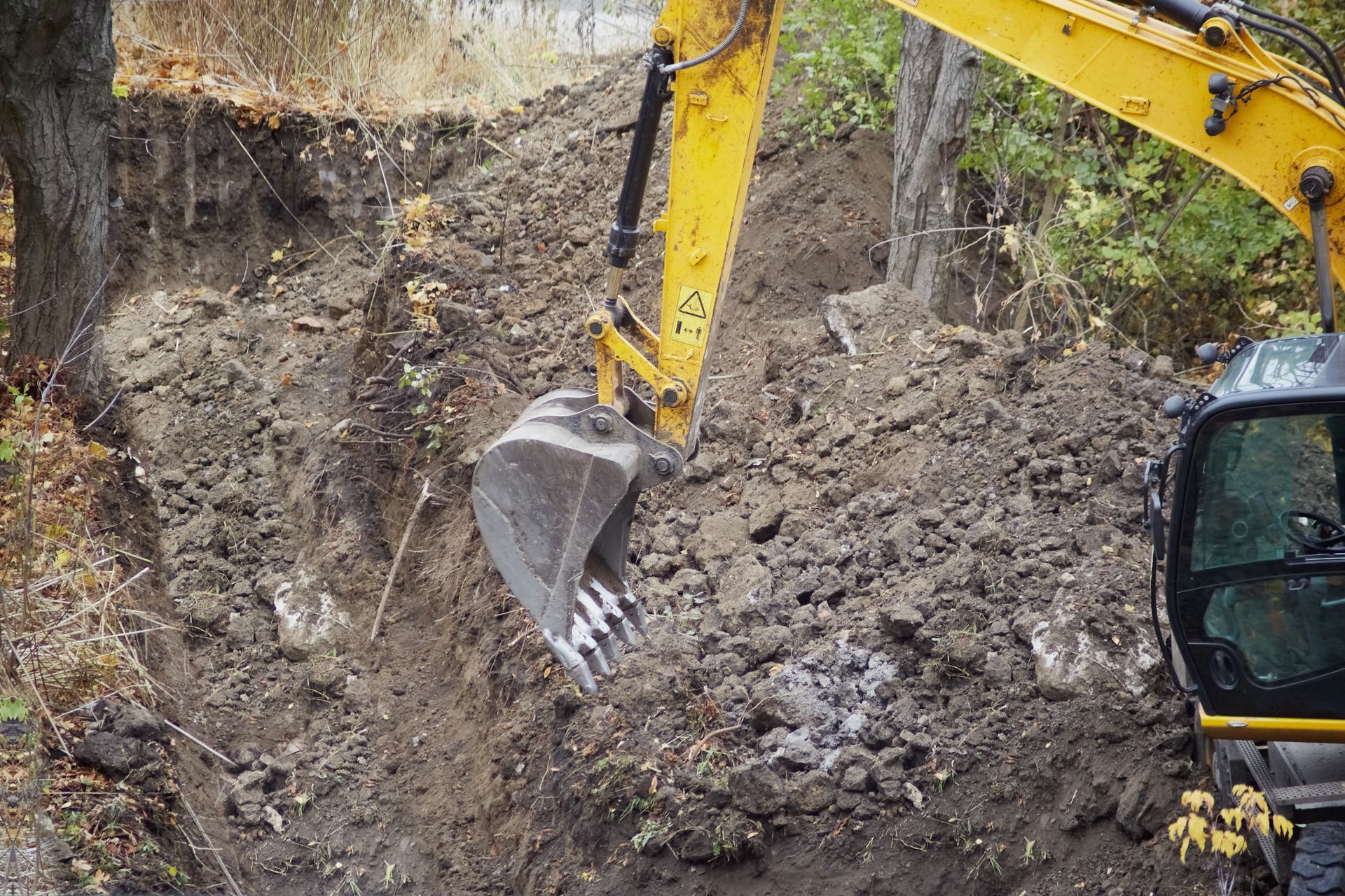 Yellow excavator digging into a rocky dirt embankment on a steep hillside.