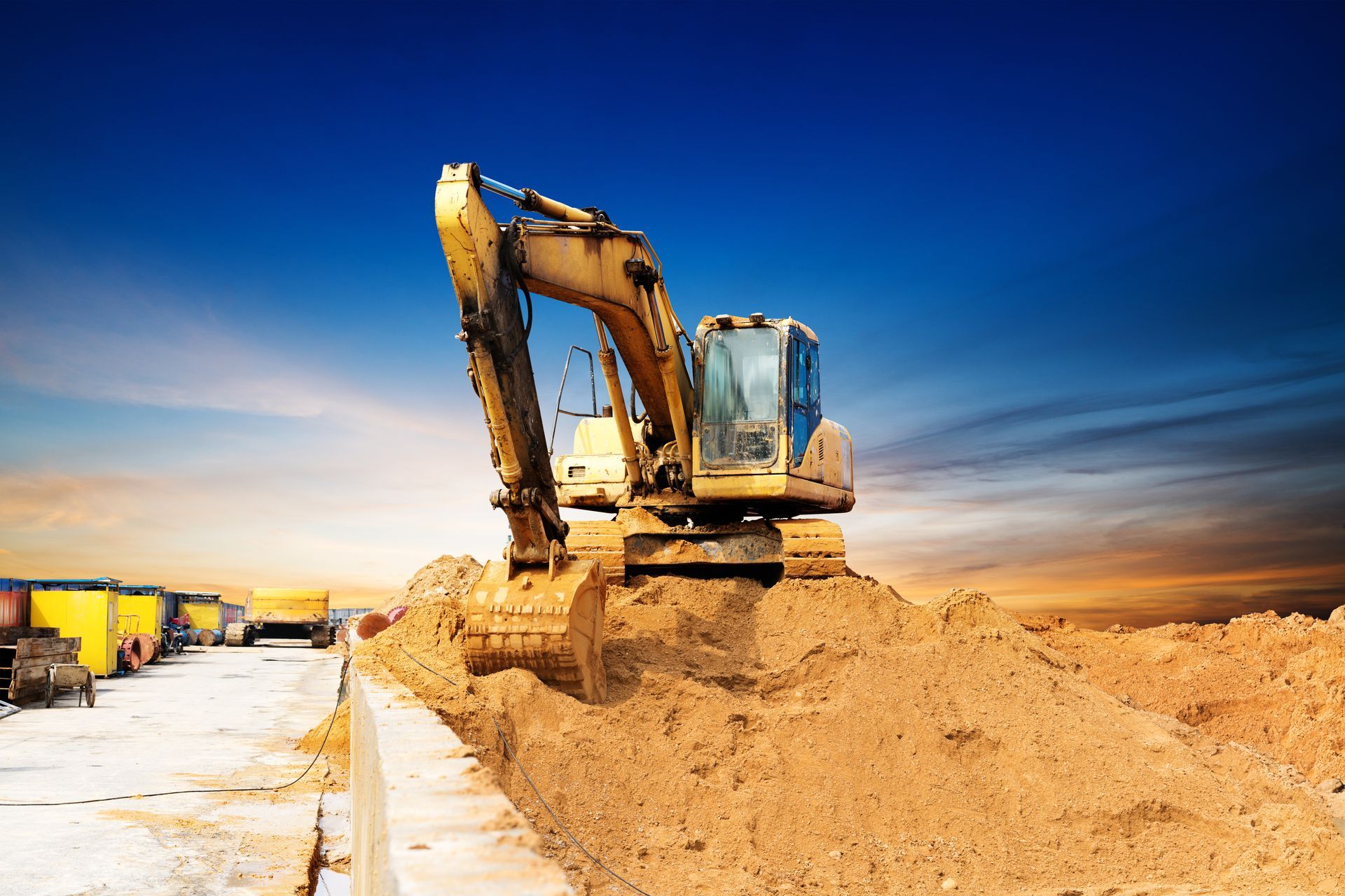 Excavator piling dirt beside a construction site under a blue sky
