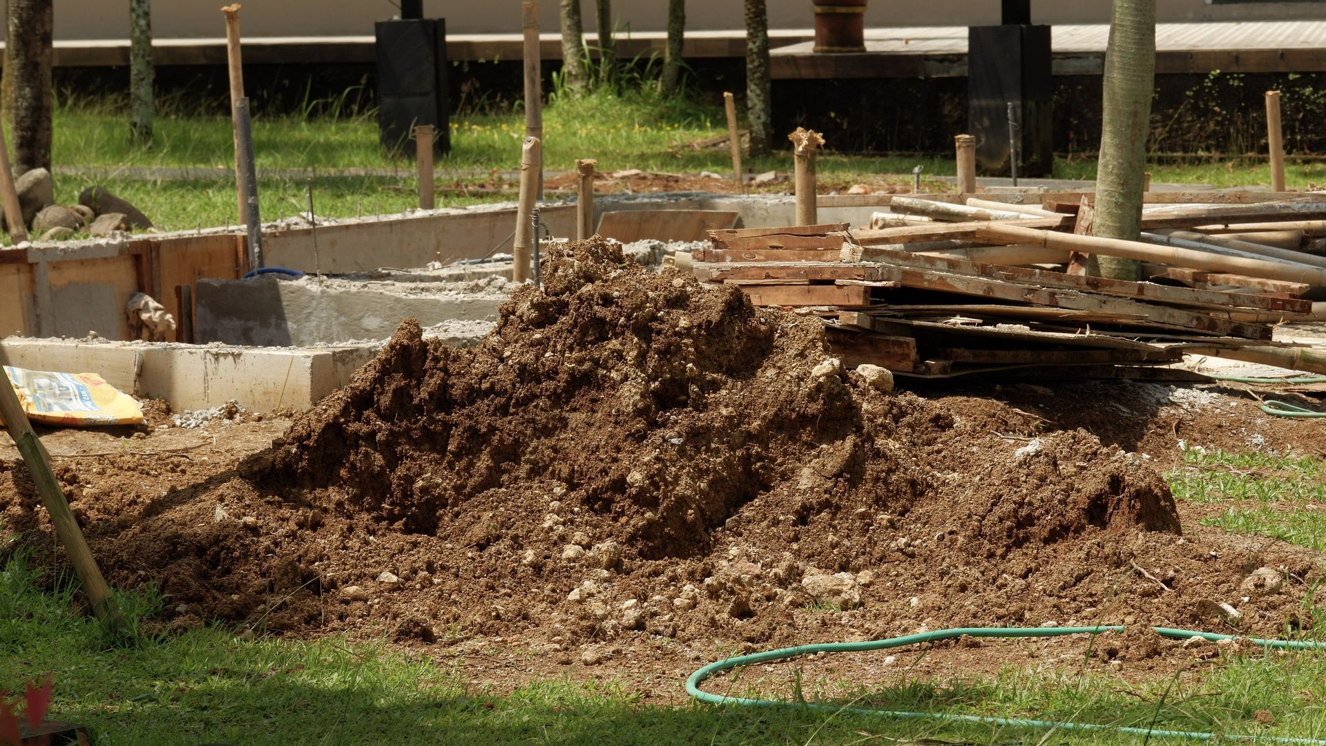 Pile of dirt and wooden planks at a construction site with a green hose in the foreground