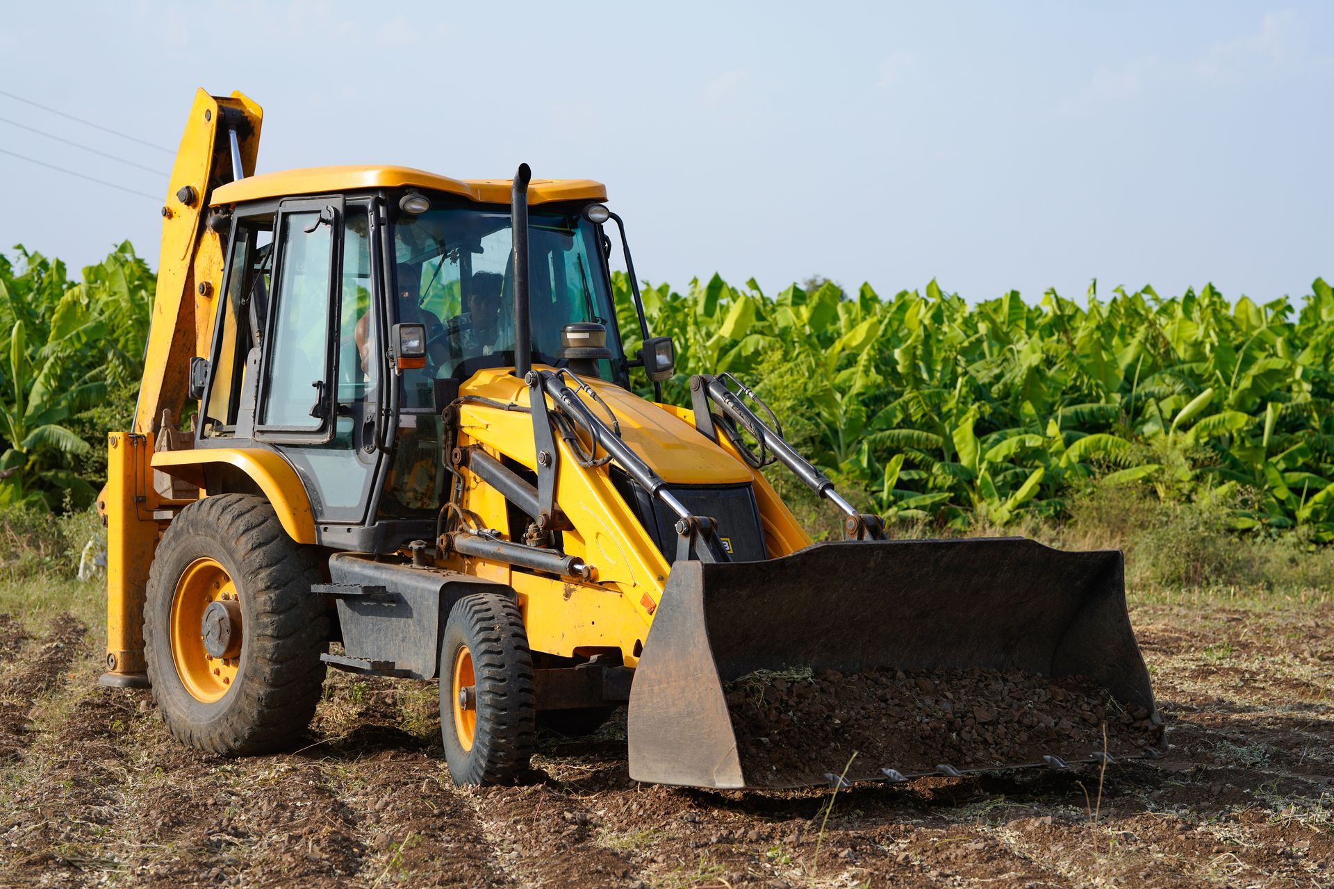 Yellow excavator digging soil at a construction site in front of a steel-framed building