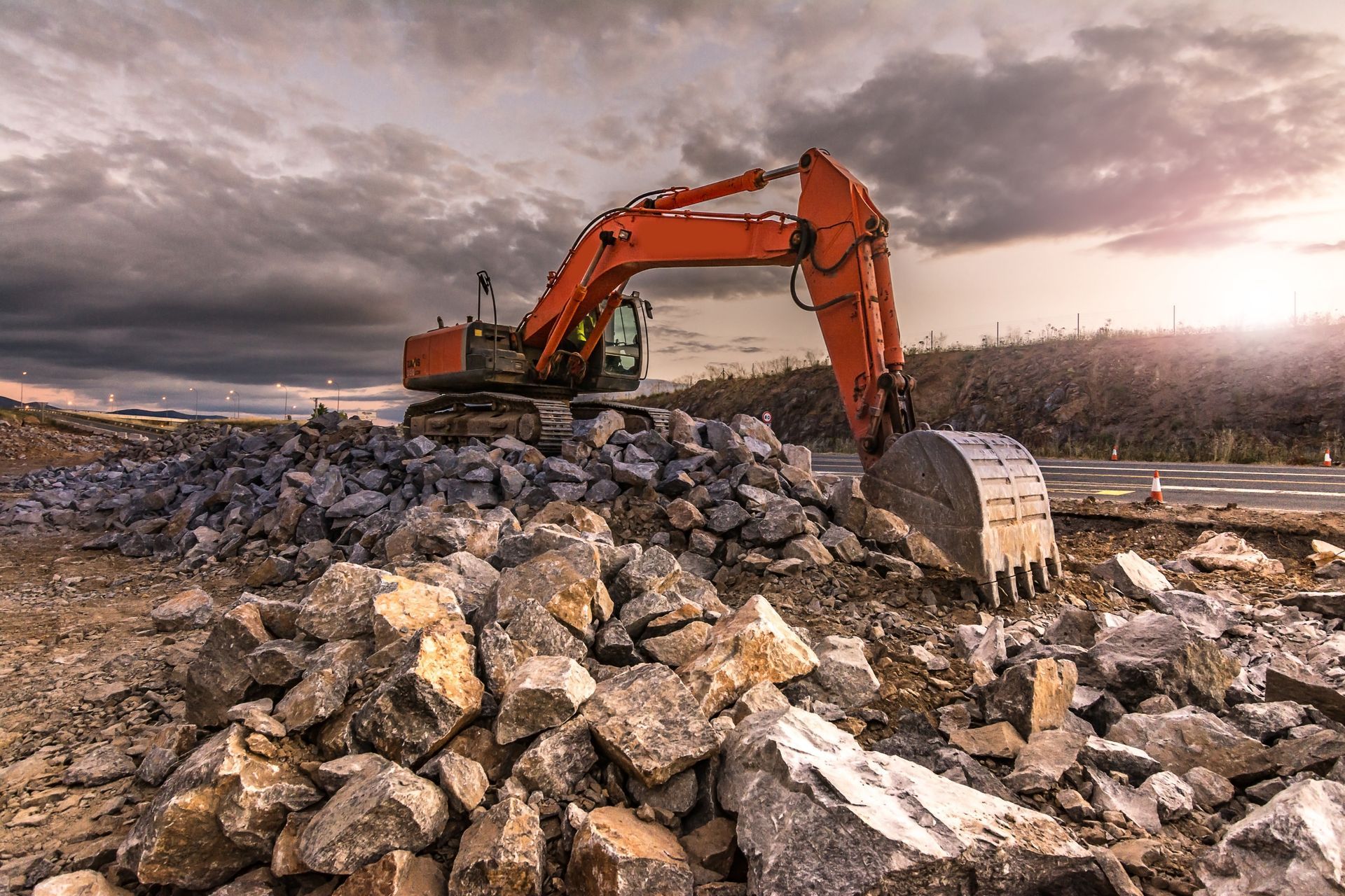 Orange excavator moving rubble on a rocky construction site under a cloudy sky