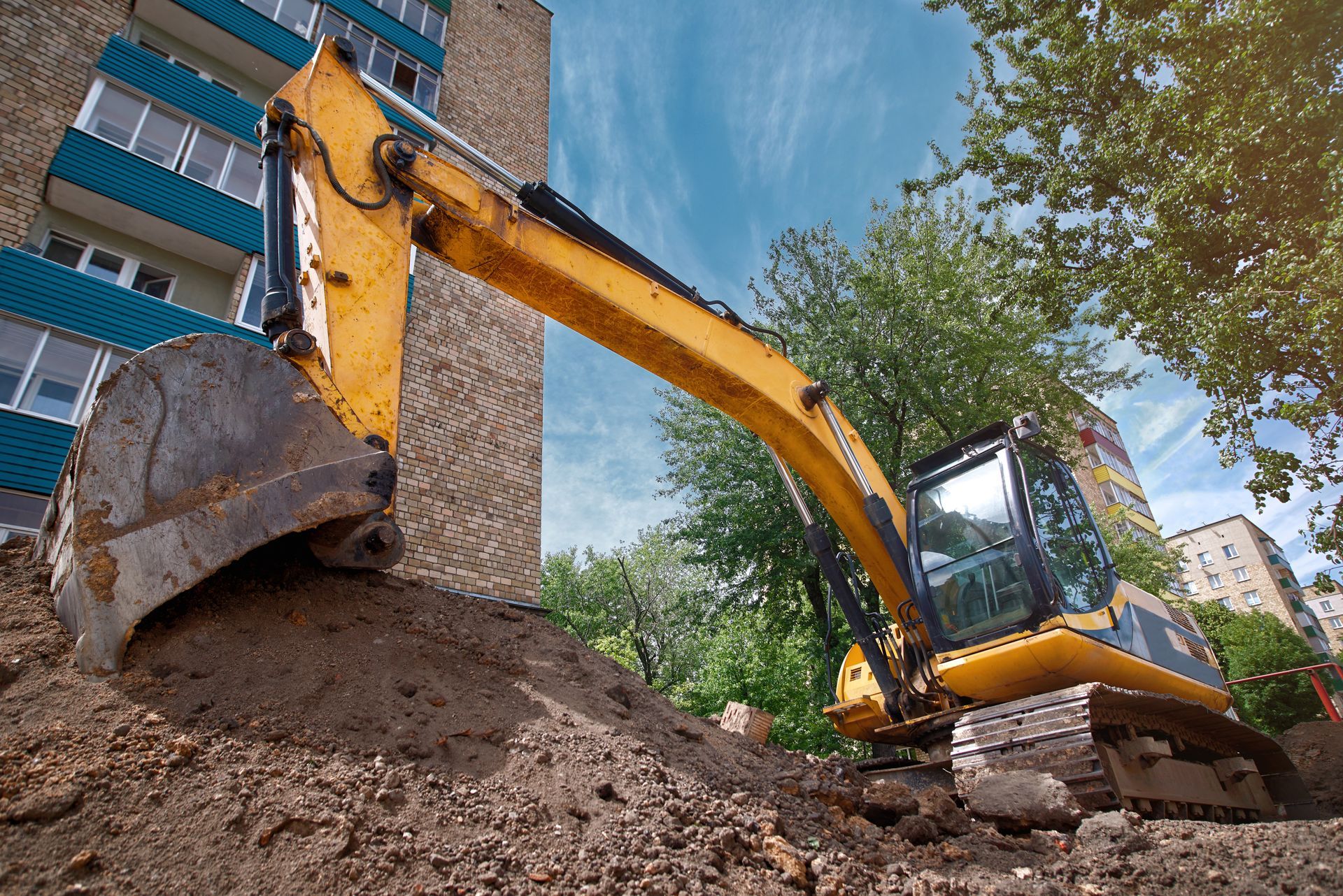 Yellow excavator digging soil beside a building on a construction site