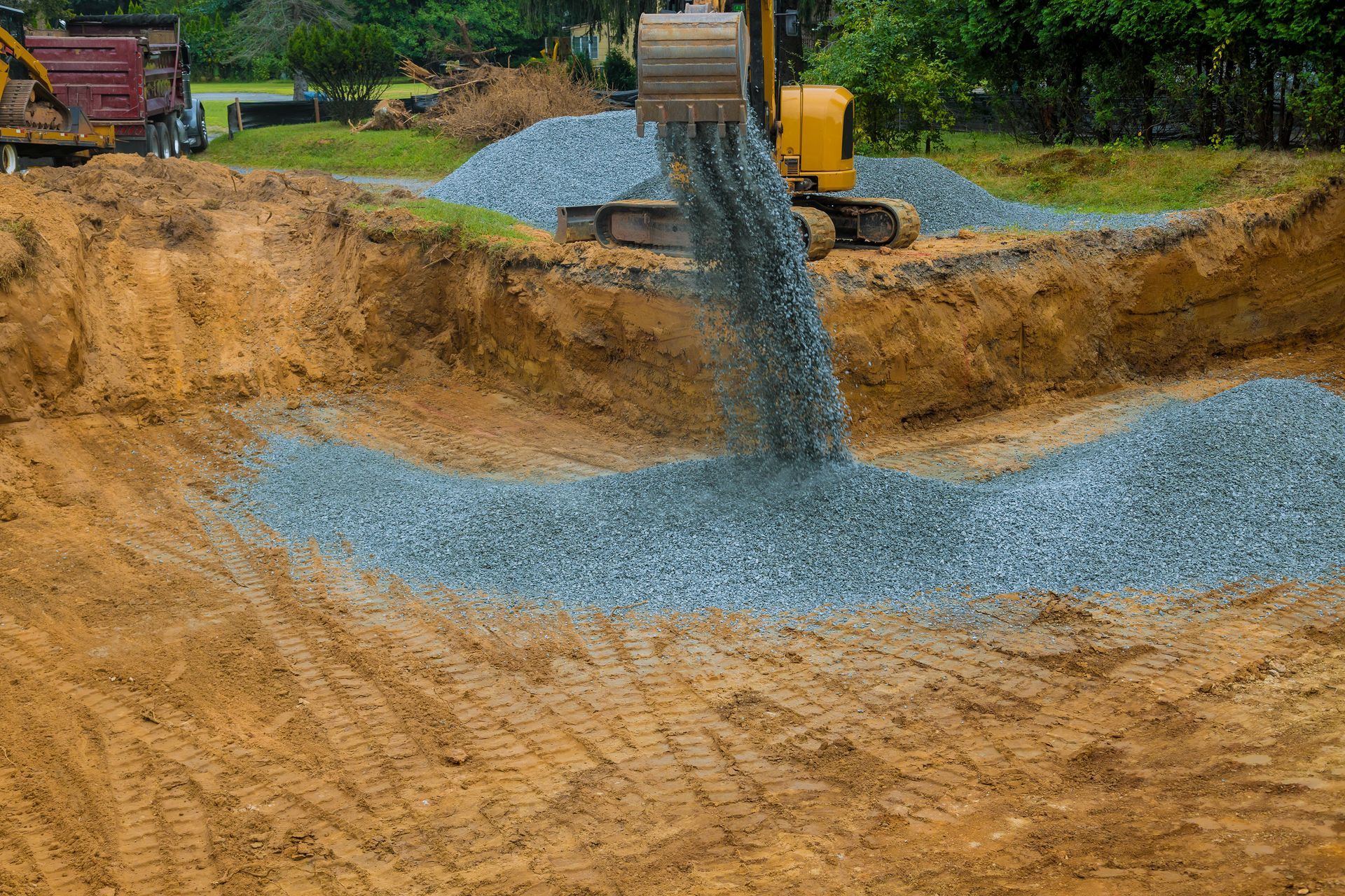 Construction site with gravel being dumped into a sandy excavation by a truck