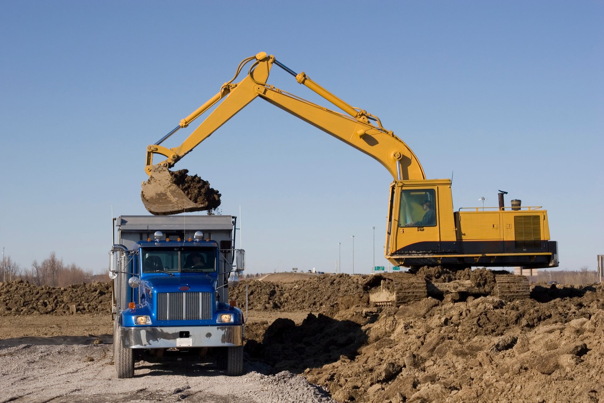 Yellow excavator loading dirt into a blue dump truck at a construction site
