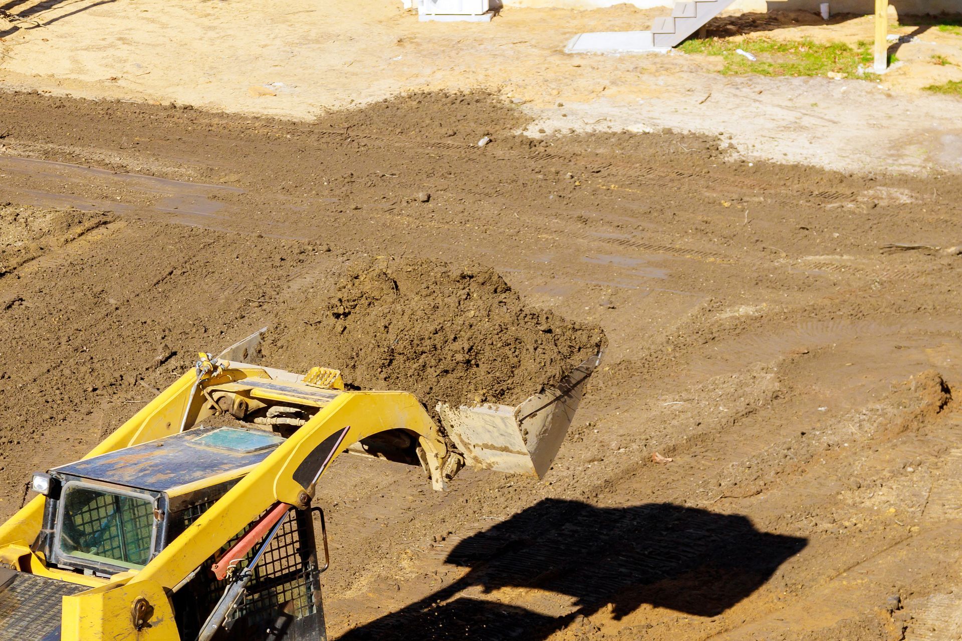 Yellow construction vehicle dumping dirt in a muddy dirt lot
