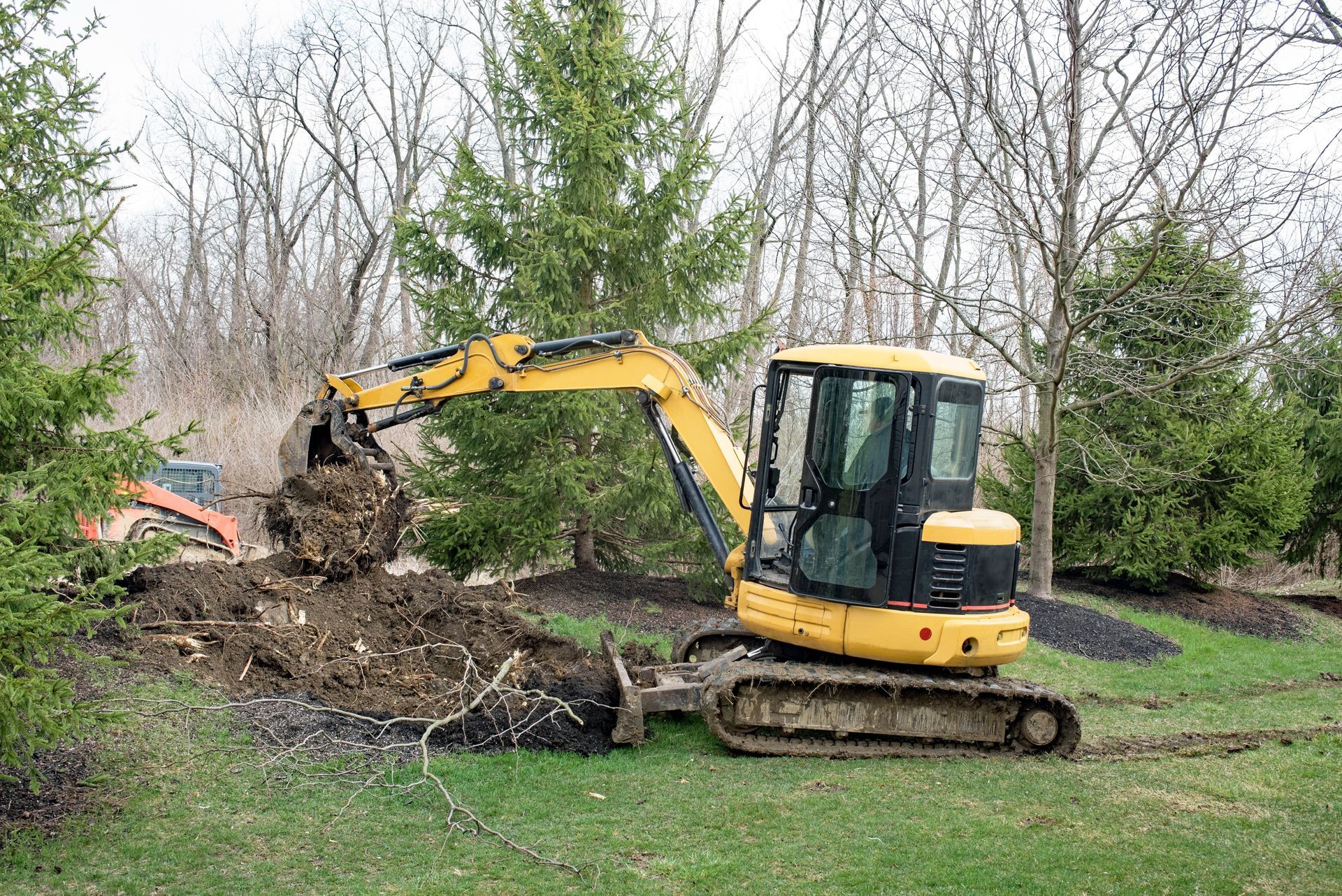 Yellow excavator digging dirt beside trees in a grassy yard
