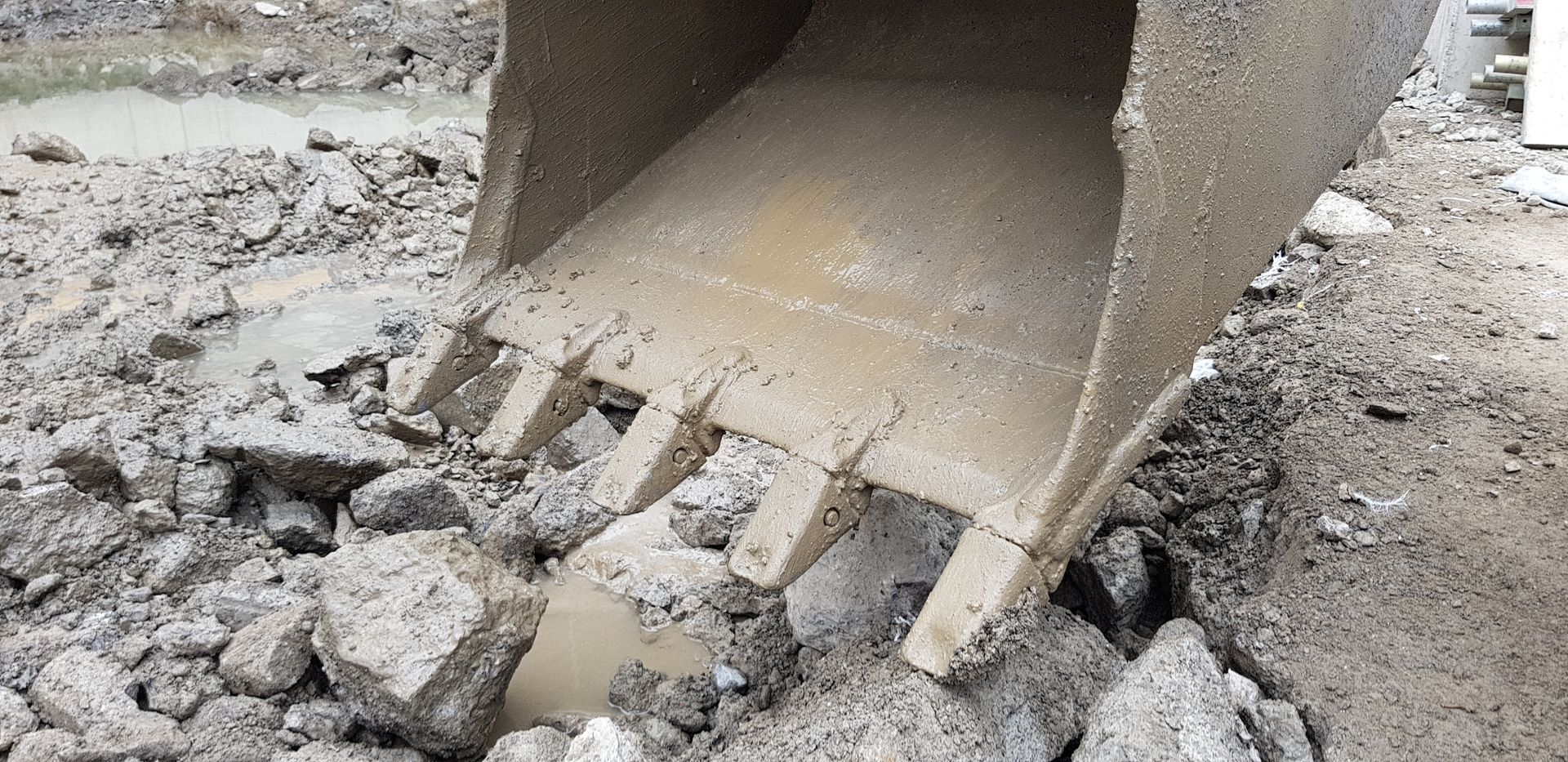 Excavator bucket breaking up gray concrete rubble on a construction site