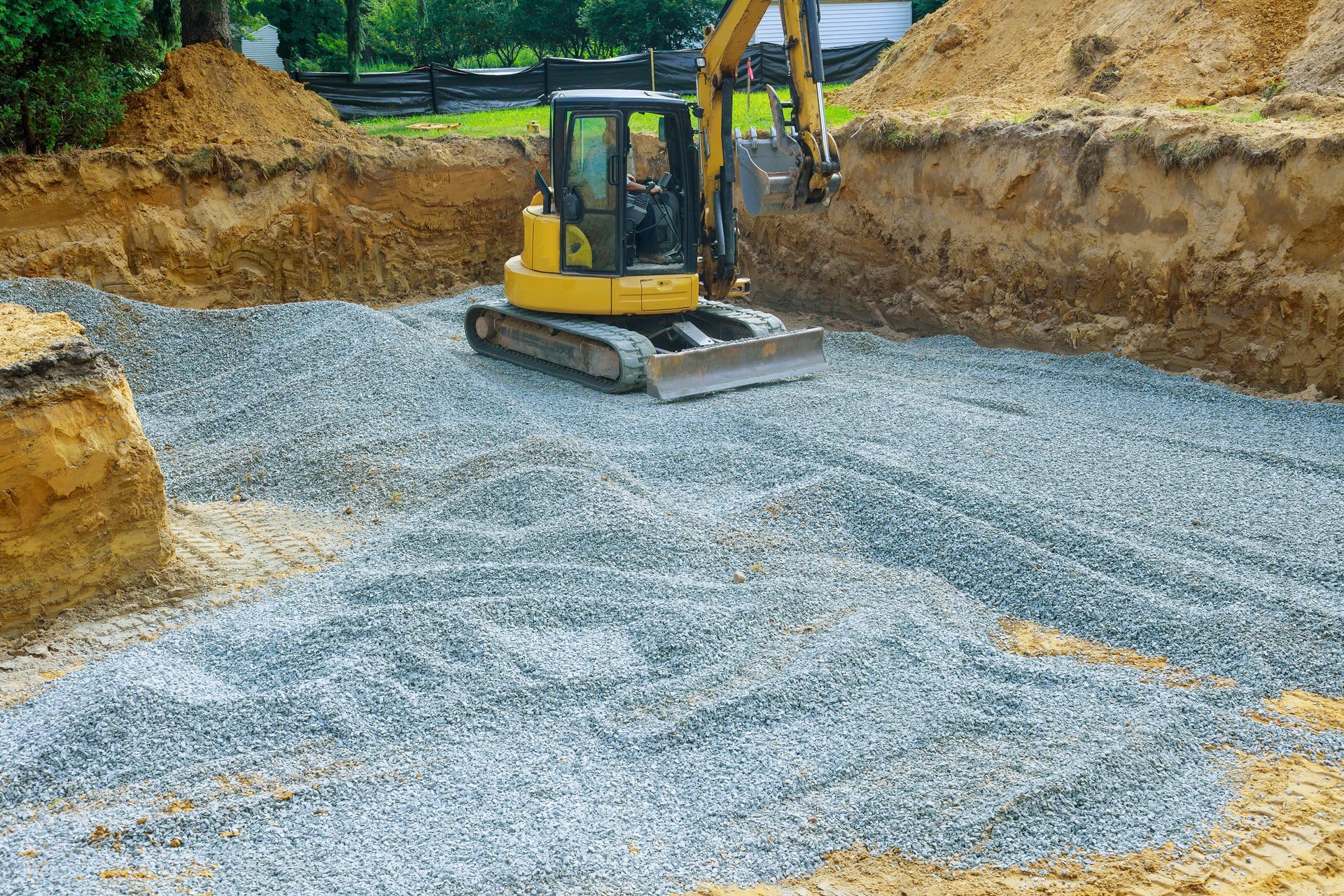 Yellow excavator leveling gravel at a construction site surrounded by dirt embankments