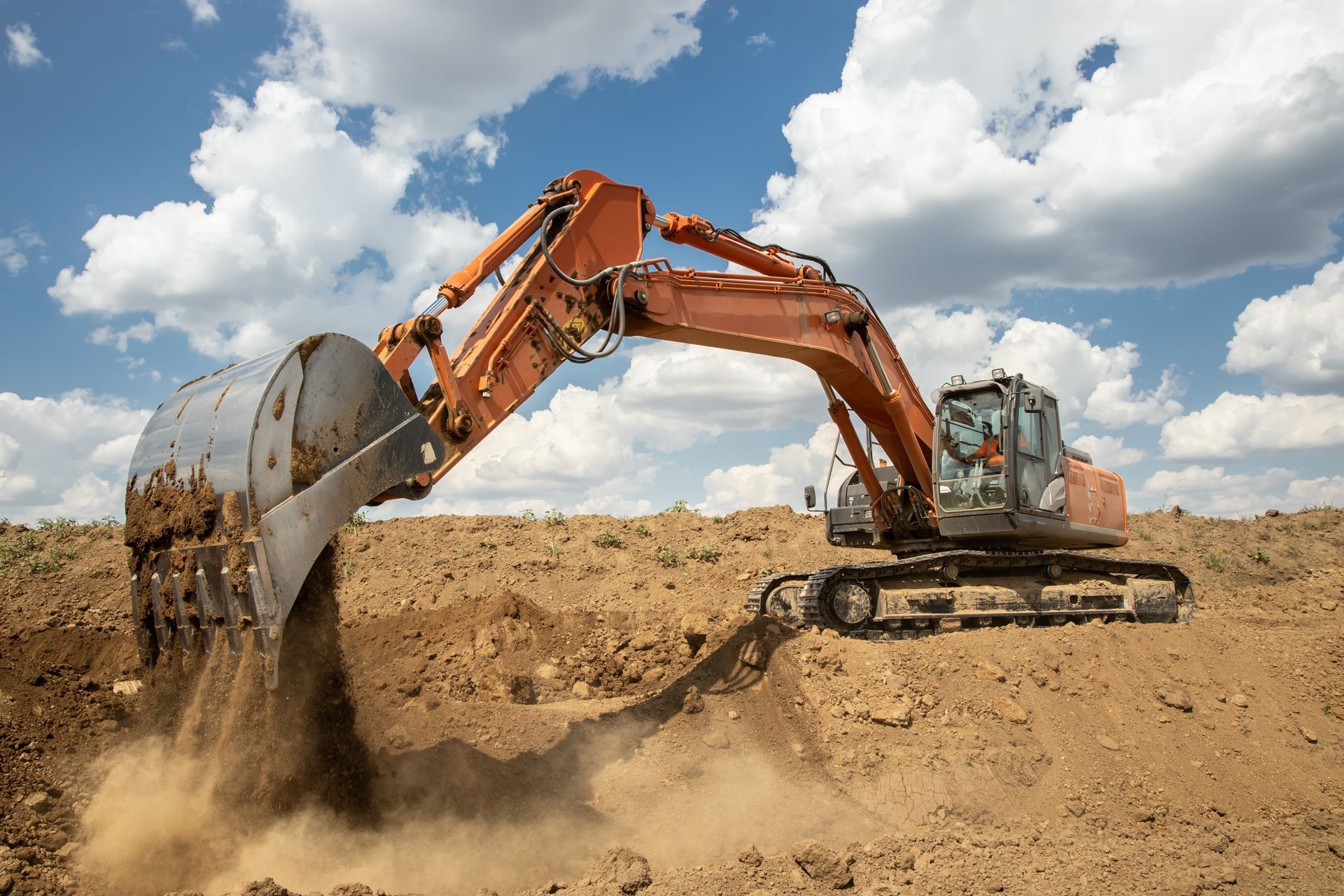 Orange excavator digging soil at a construction site under a blue sky with clouds