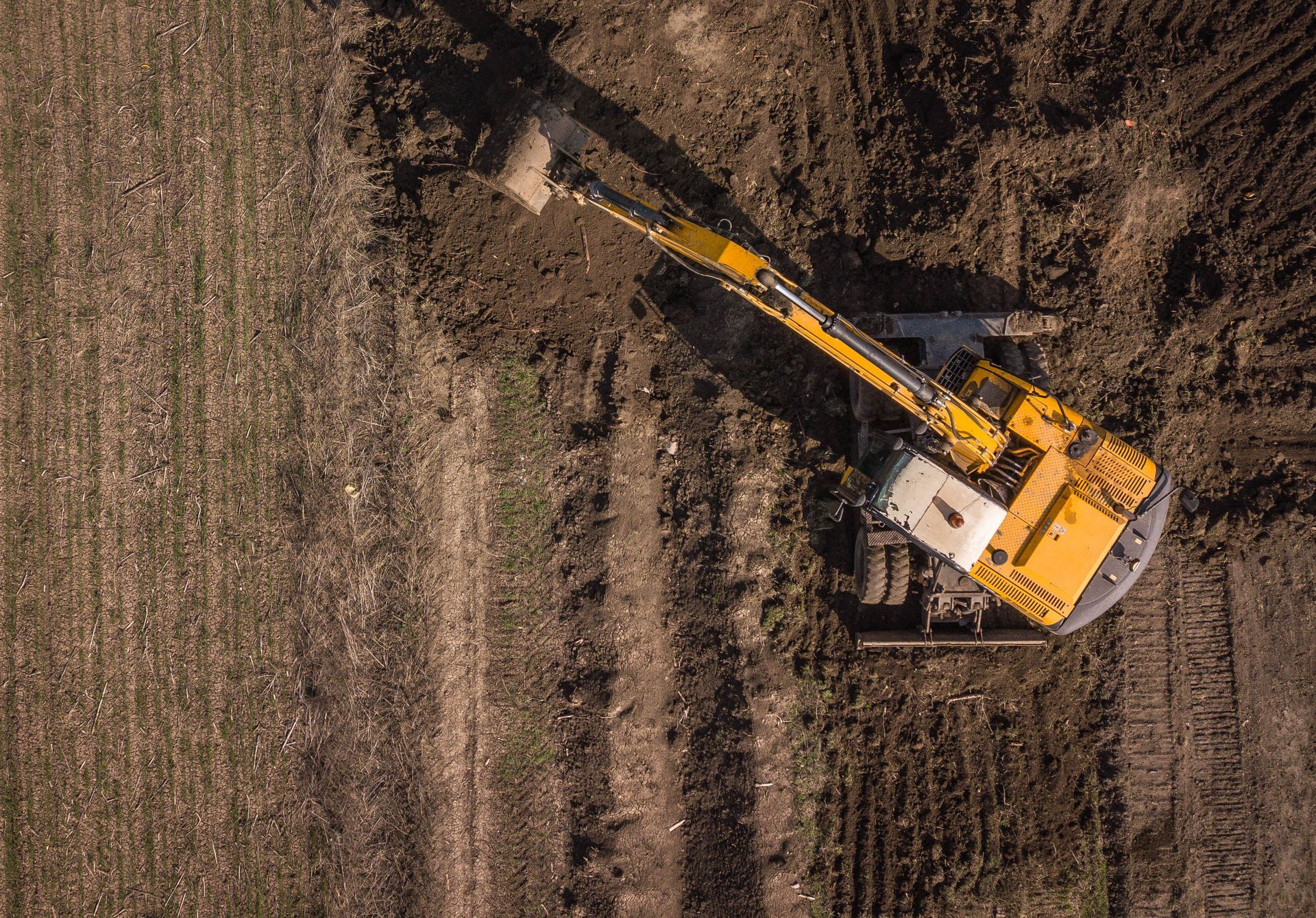 Aerial view of a yellow excavator working in a brown dirt field